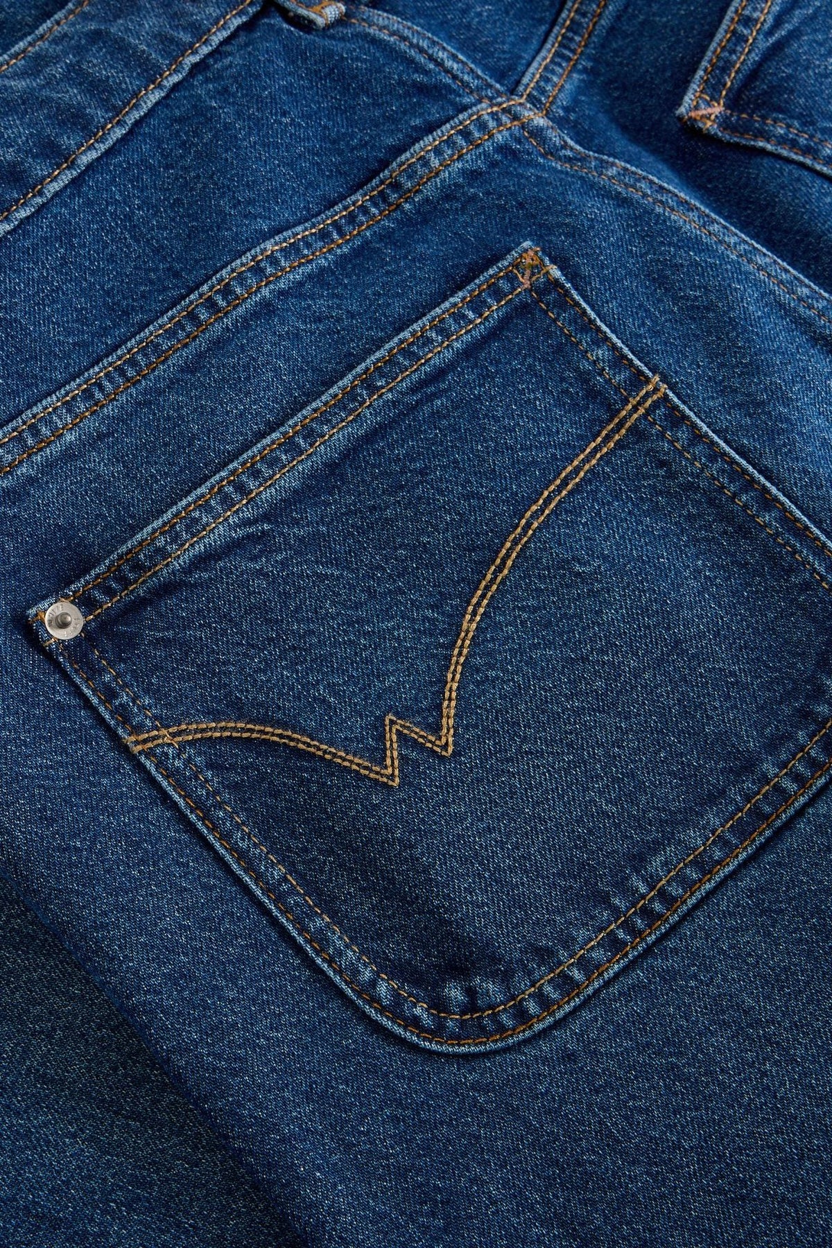 Close up of a dark denim jean pocket with signature gold stitching and silver rivet.