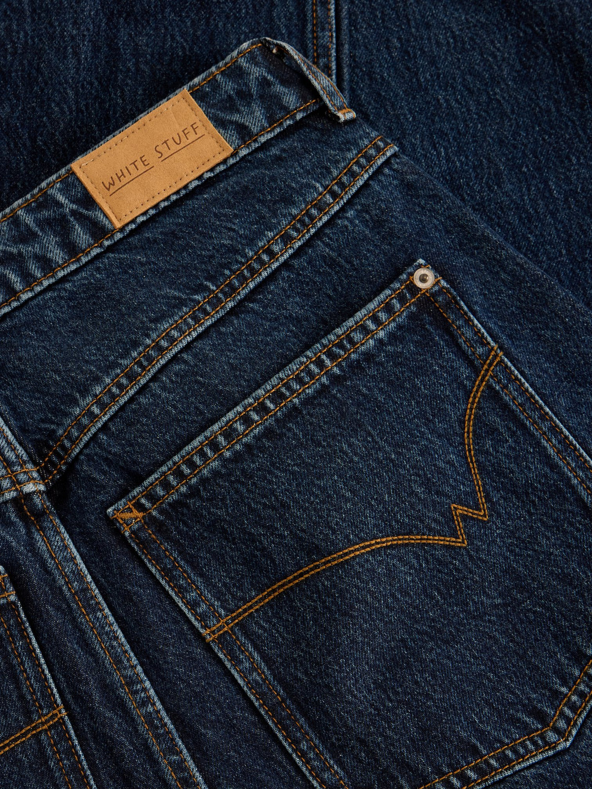 Close up of a White Stuff dark denim jeans pocket with contrast stitching and leather brand label