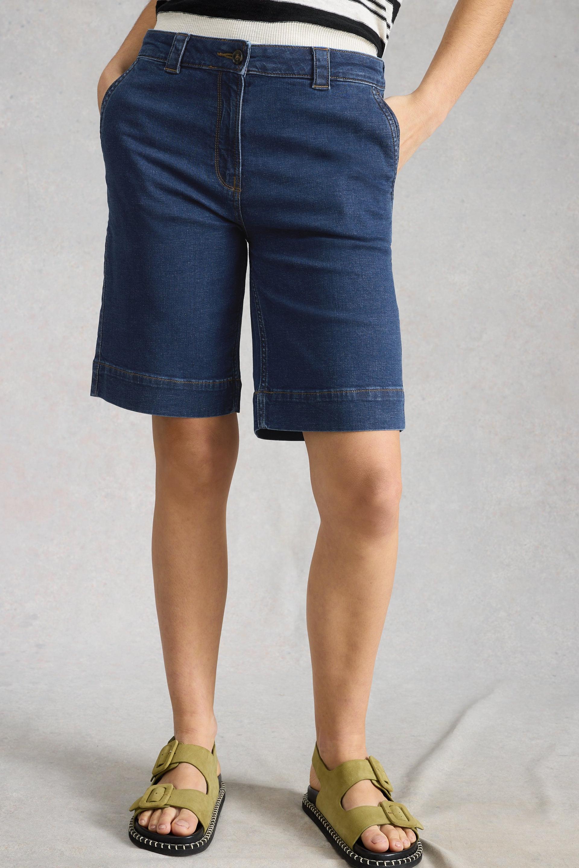 Person wearing dark blue denim shorts on a plain background