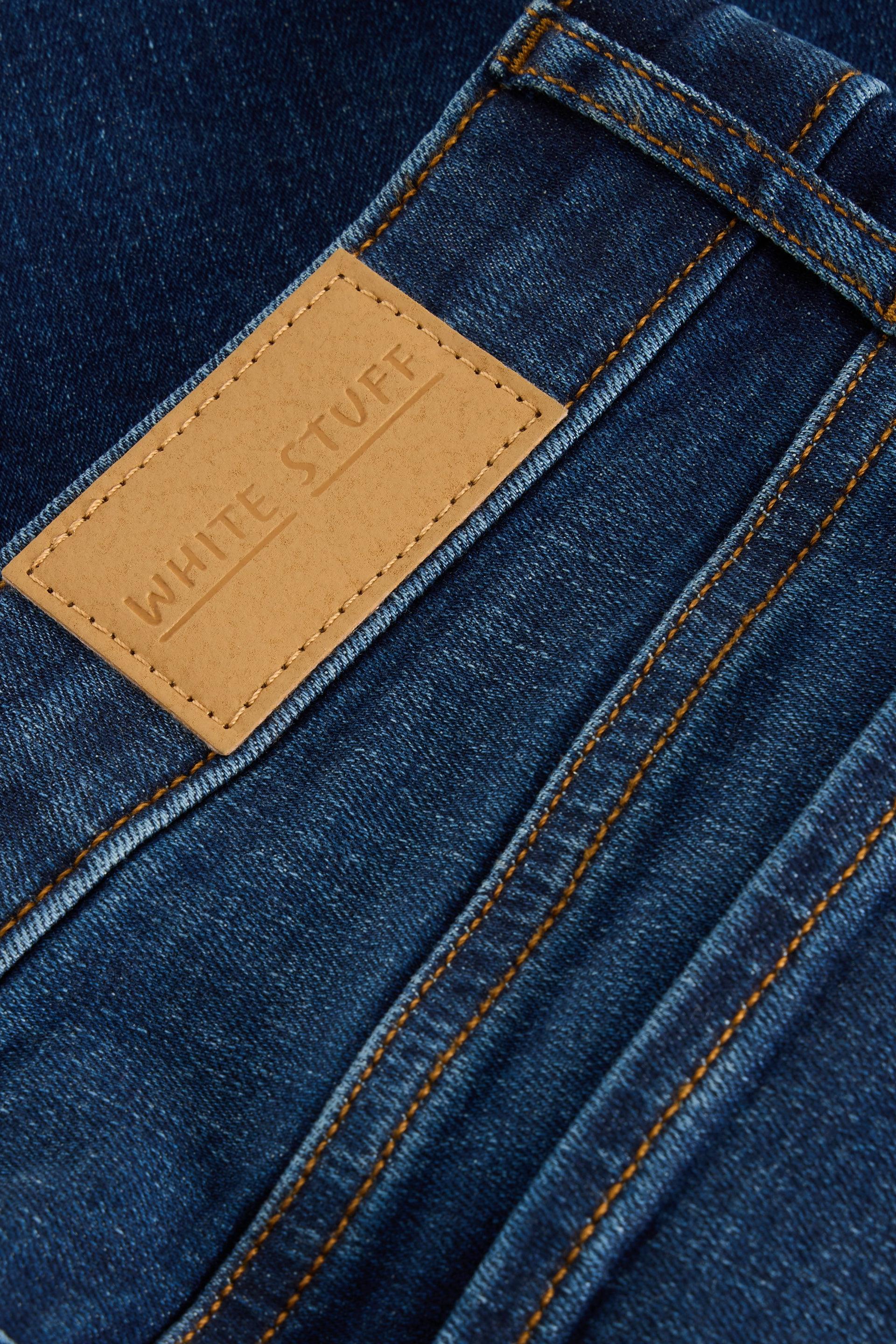 Close-up of a White Stuff brand leather patch on dark blue denim bootcut jeans.