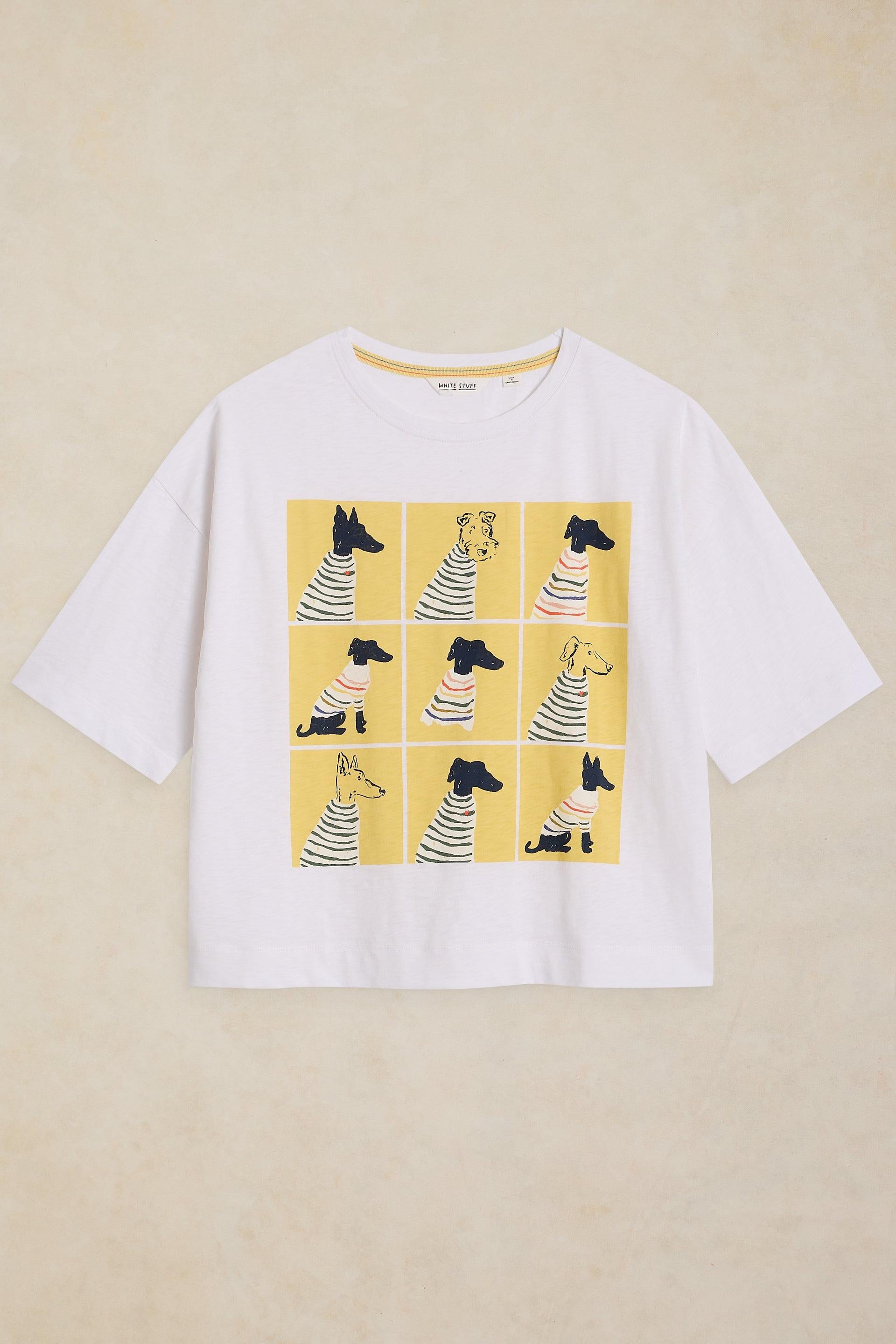 A white short-sleeve crewneck t-shirt featuring a graphic print of nine cartoon dogs in a nine-panel comic strip wearing striped shirts, set against a solid yellow background. The t-shirt is displayed flat on a textured beige background.