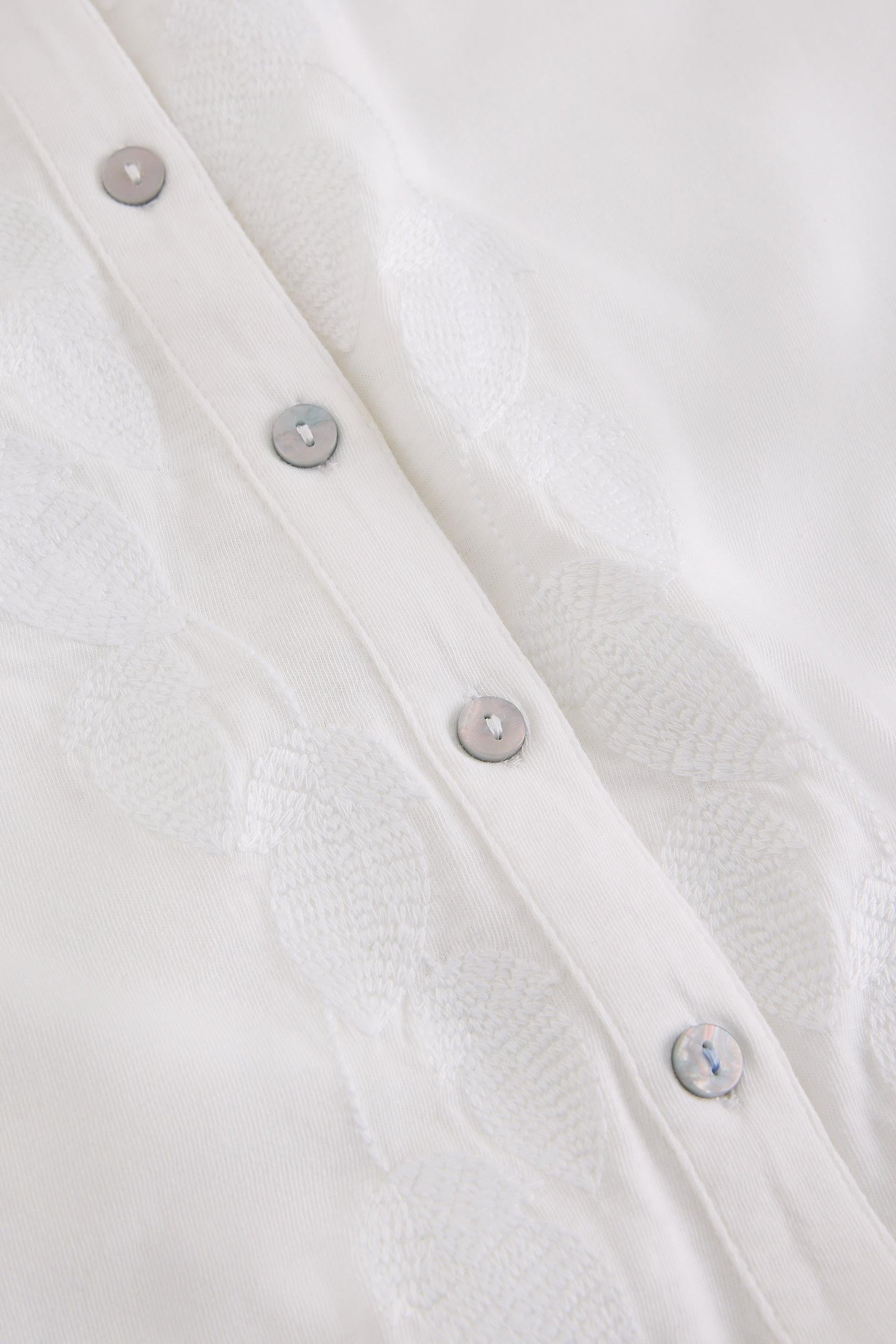 Close-up of embroidered white fabric with button details