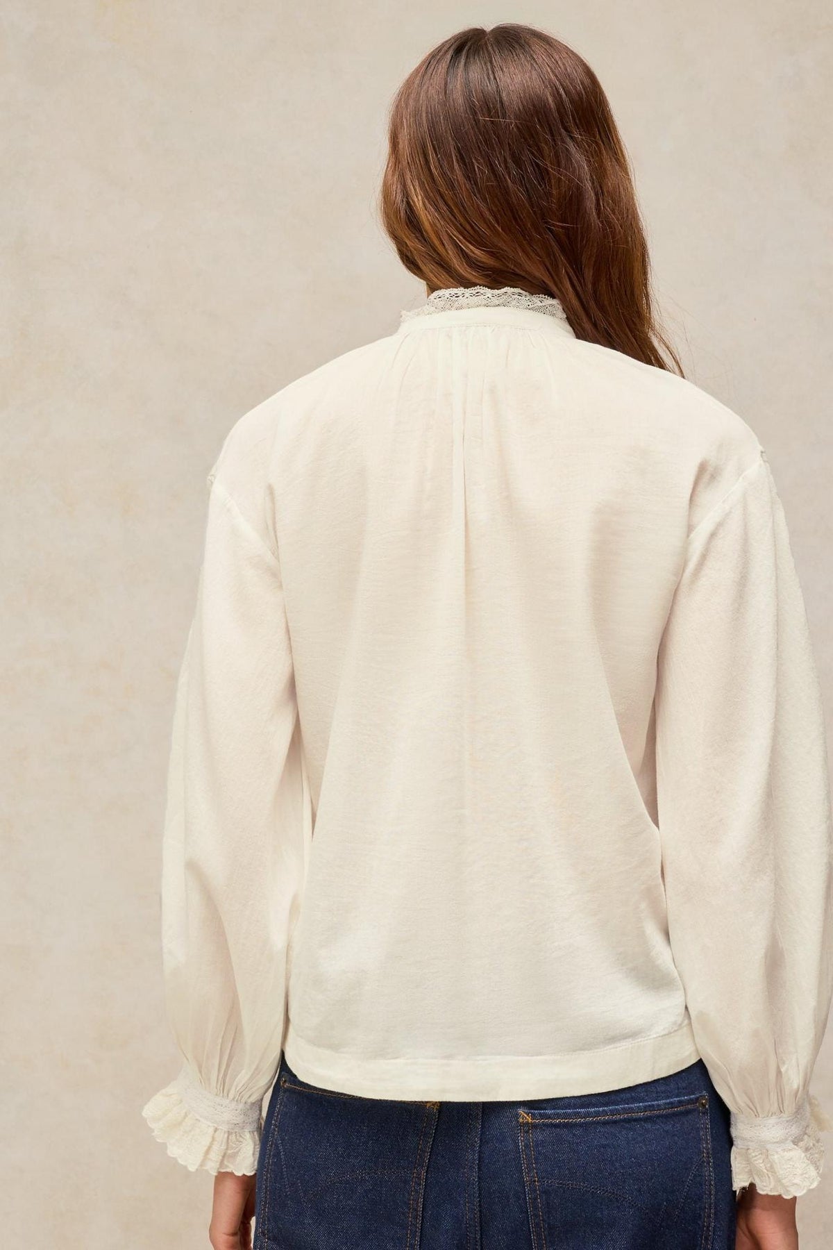 Rear view of a woman wearing a White Stuff long-sleeved embroidered organic cotton white blouse with lace cuffs.