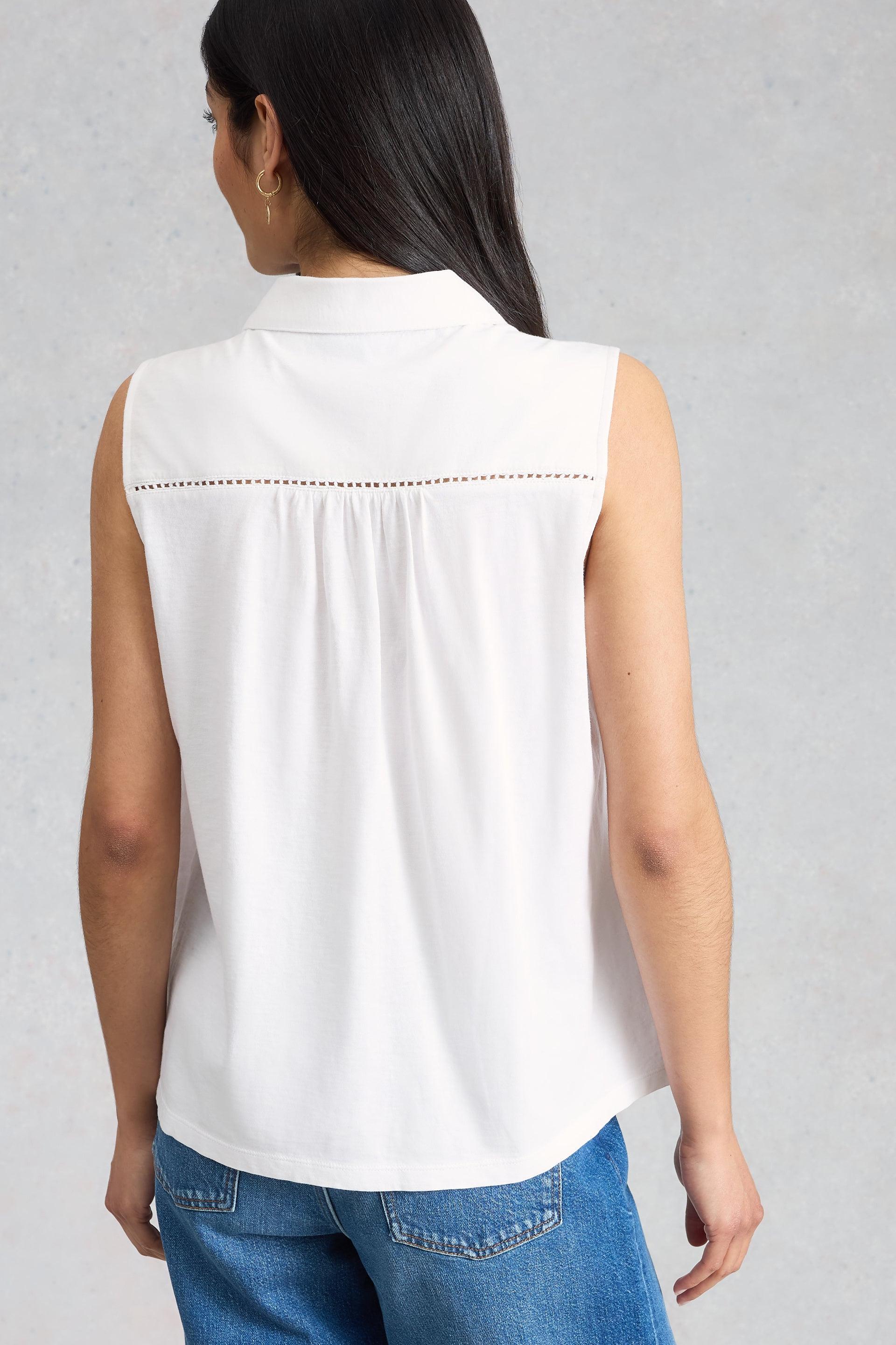 Woman wearing a white sleeveless blouse with decorative stitching on a gray background