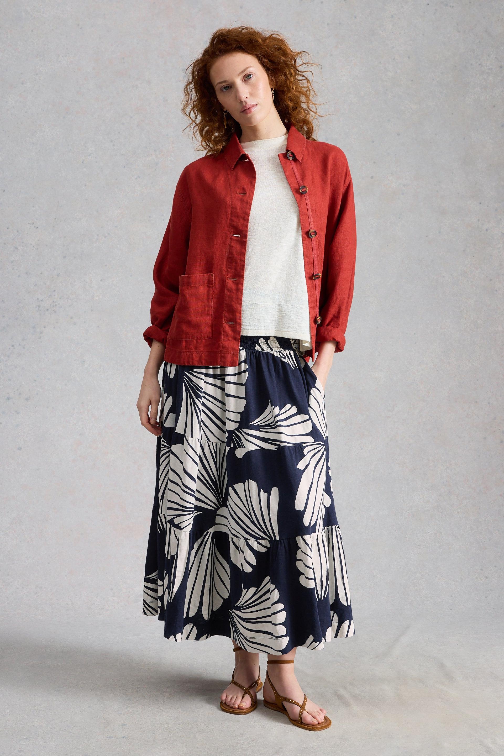 Woman wearing a red denim jacket, white top, and navy printed tiered skirt on a gray background