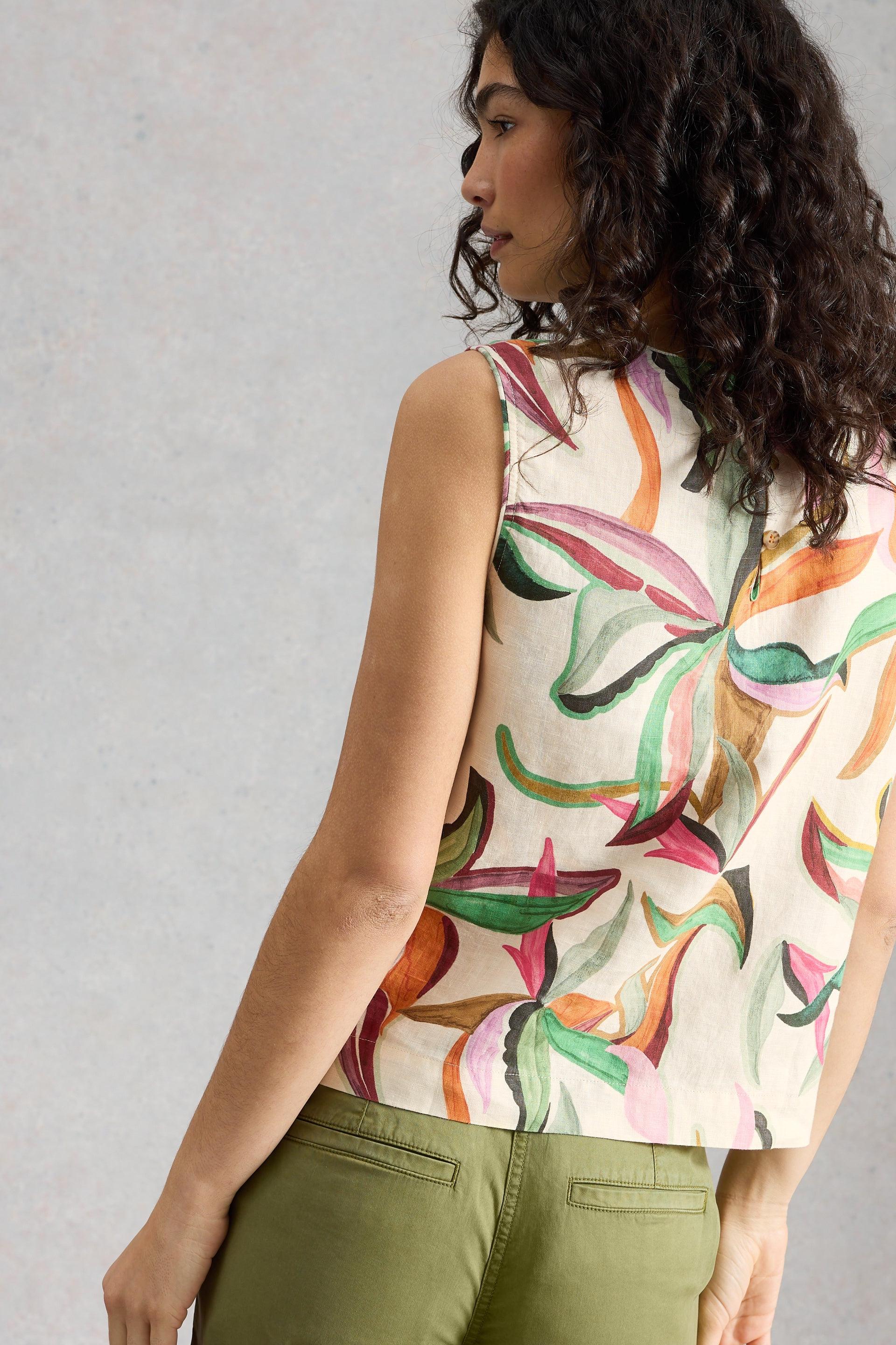 Woman wearing a sleeveless top with coloruful abstract design against a plain background