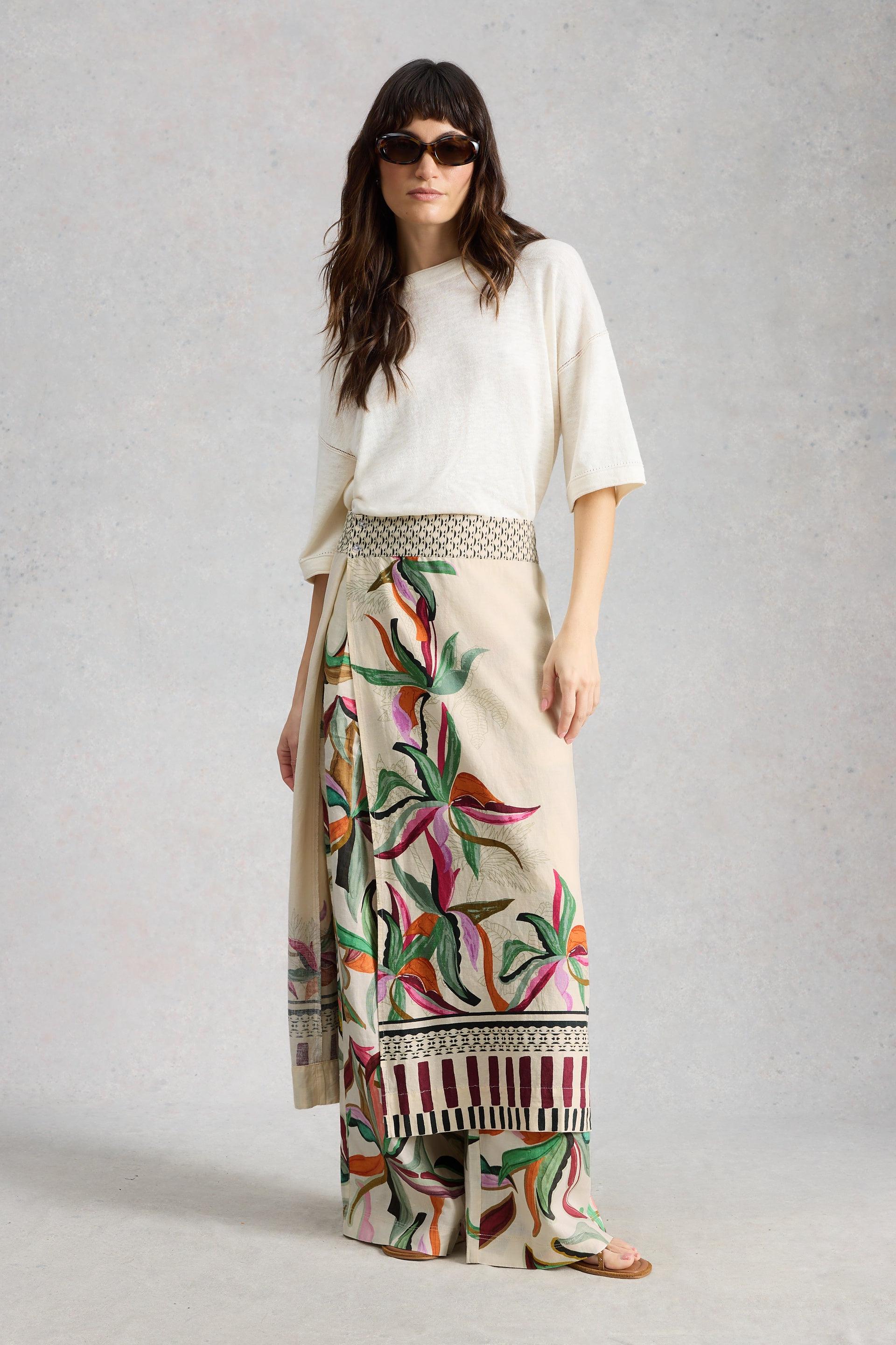 Woman wearing a white top and colorful patterned skirt on a plain background