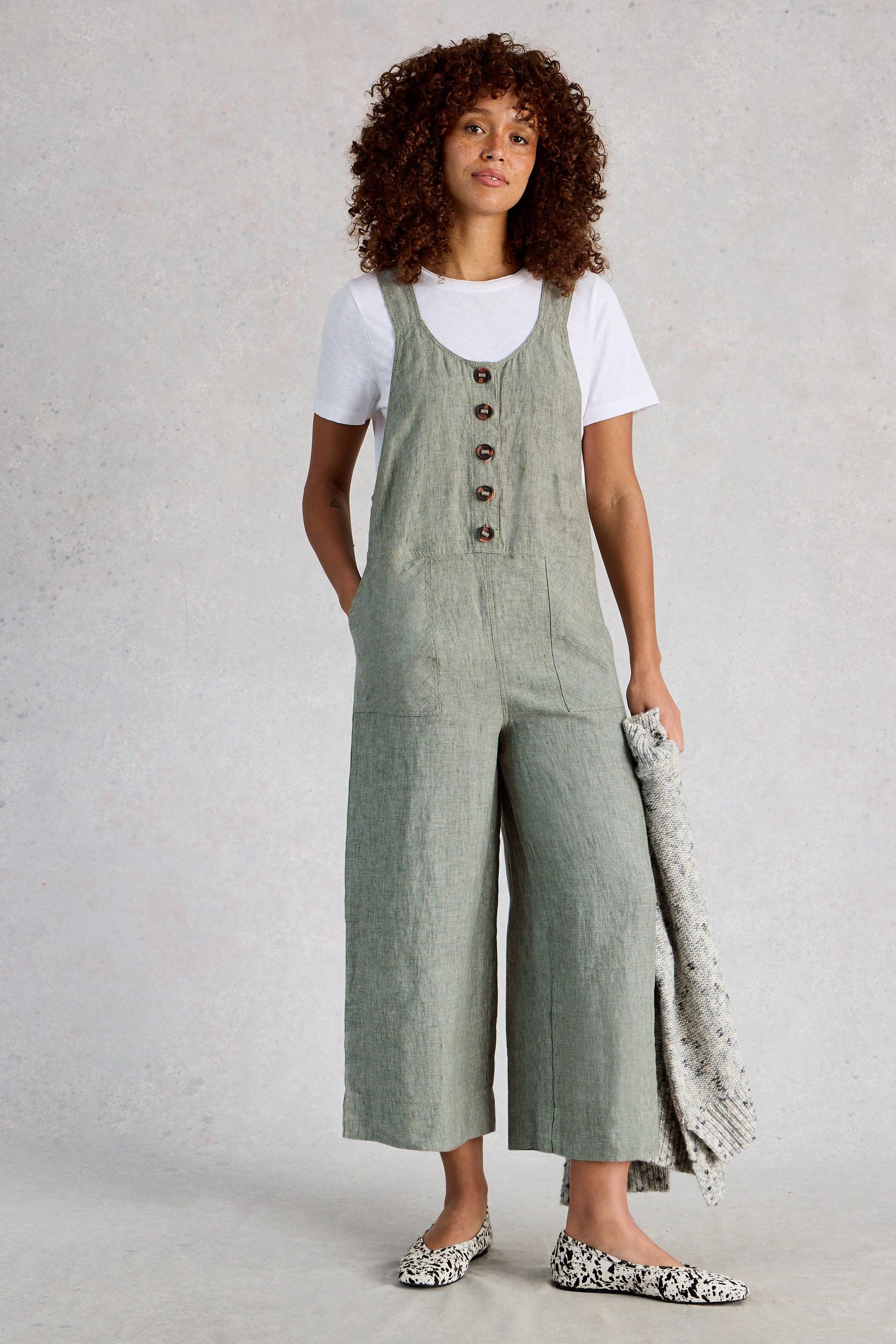 Woman wearing a green linen dungarees with a white shirt on a plain background