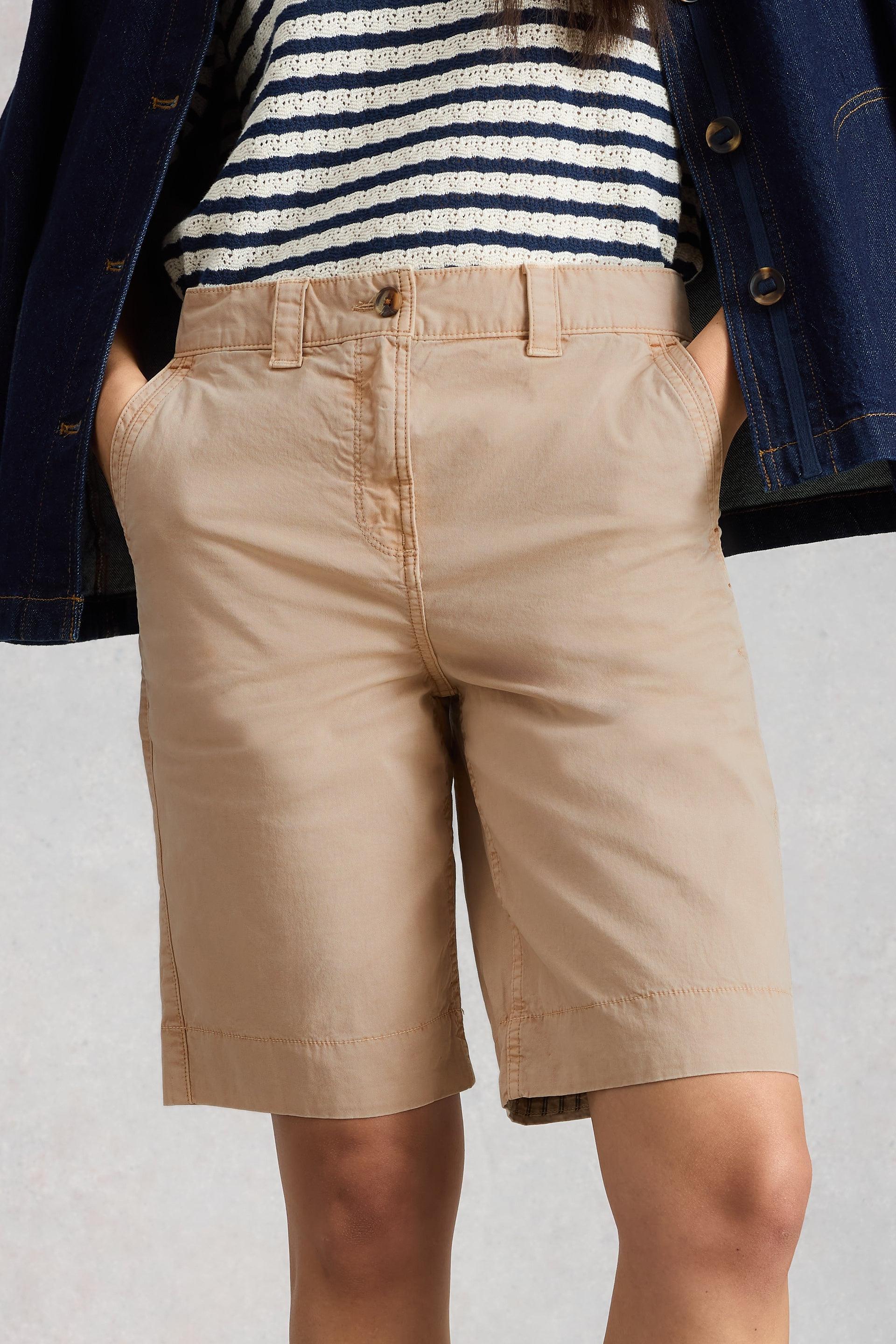Person wearing beige organic cotton shorts and a striped shirt with a blue jacket on a light gray background