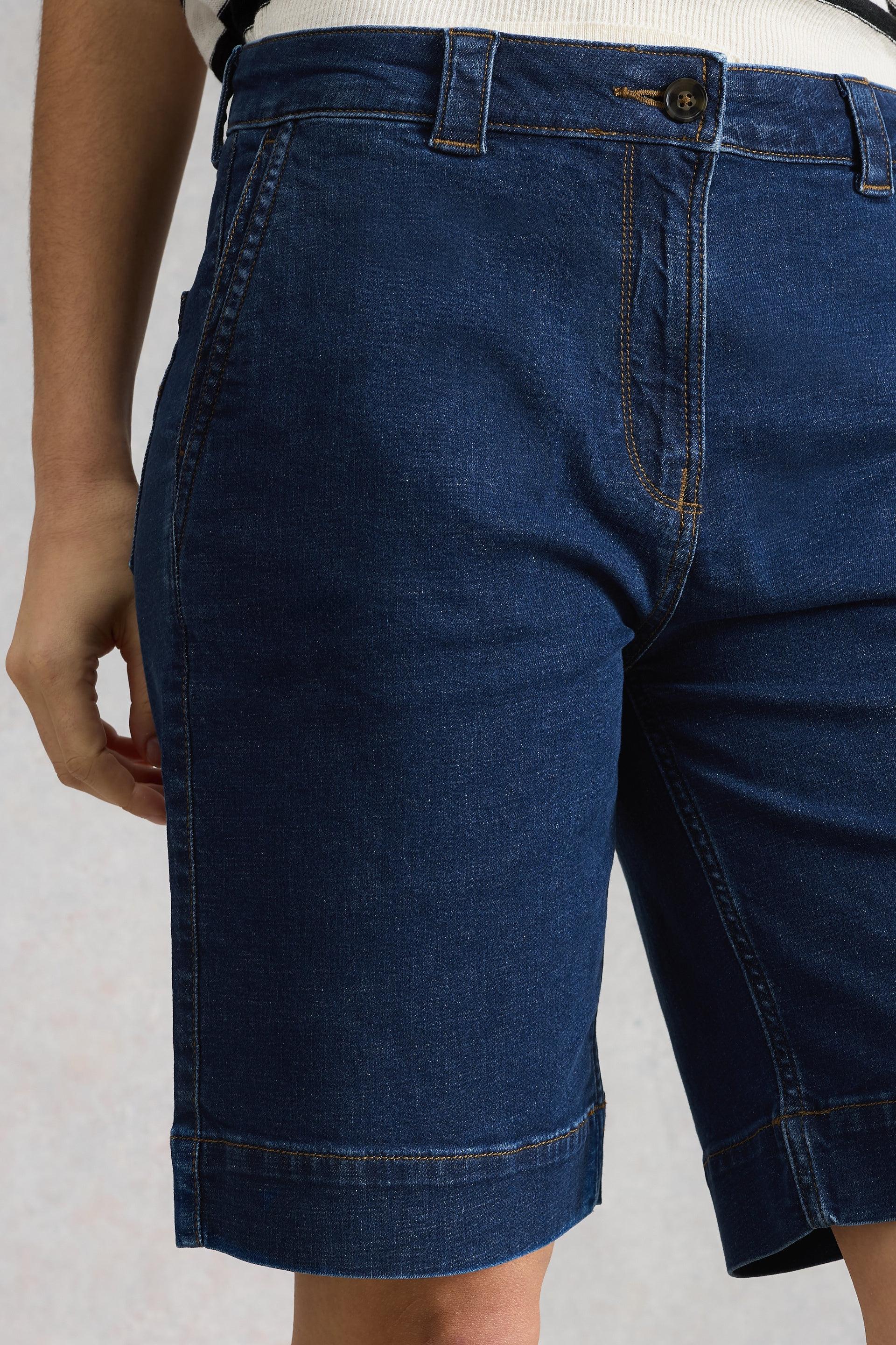 Dark blue denim shorts worn by a person on a light gray background