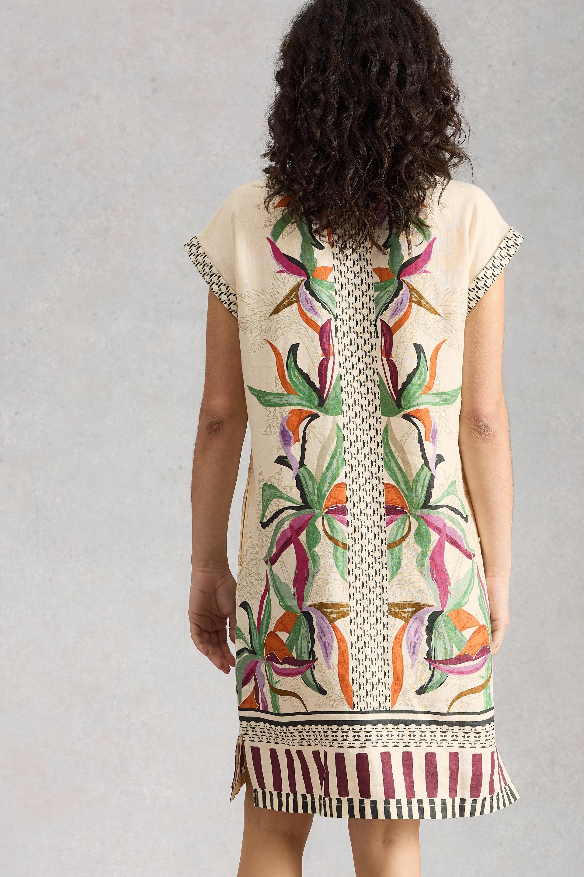 Woman wearing a sleeveless dress with colorful floral pattern on a plain background