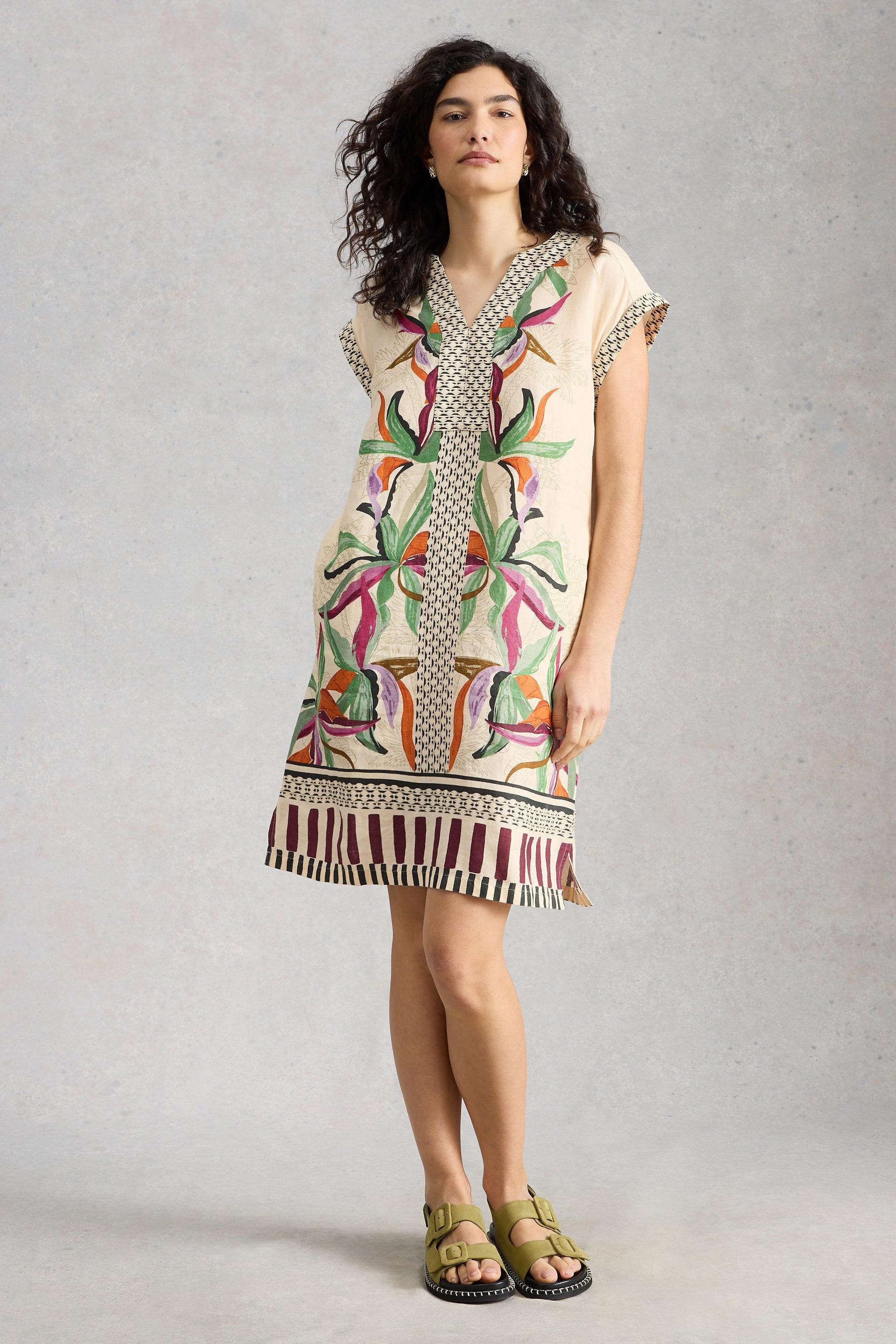 Woman wearing a beige patterned linen dress against a plain background