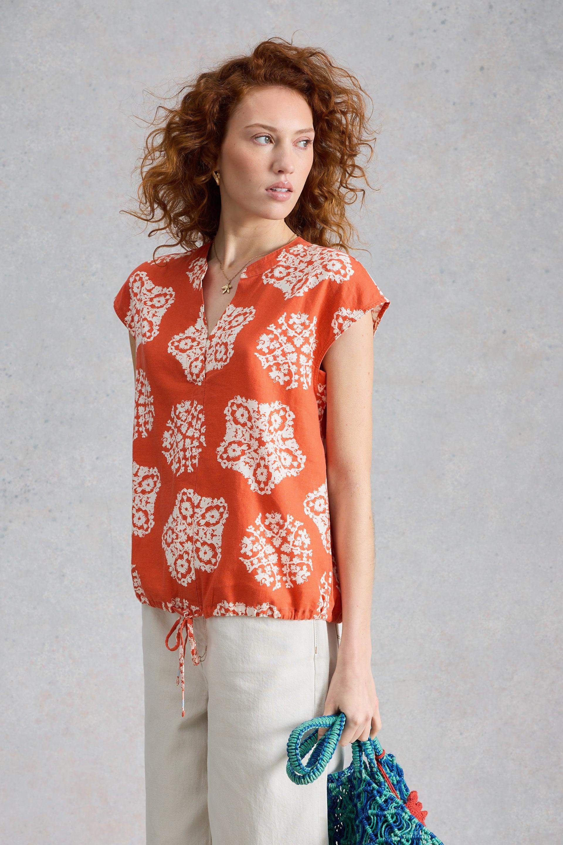 Woman wearing a red patterned top with short sleeves, notch neckline and drawstring hem