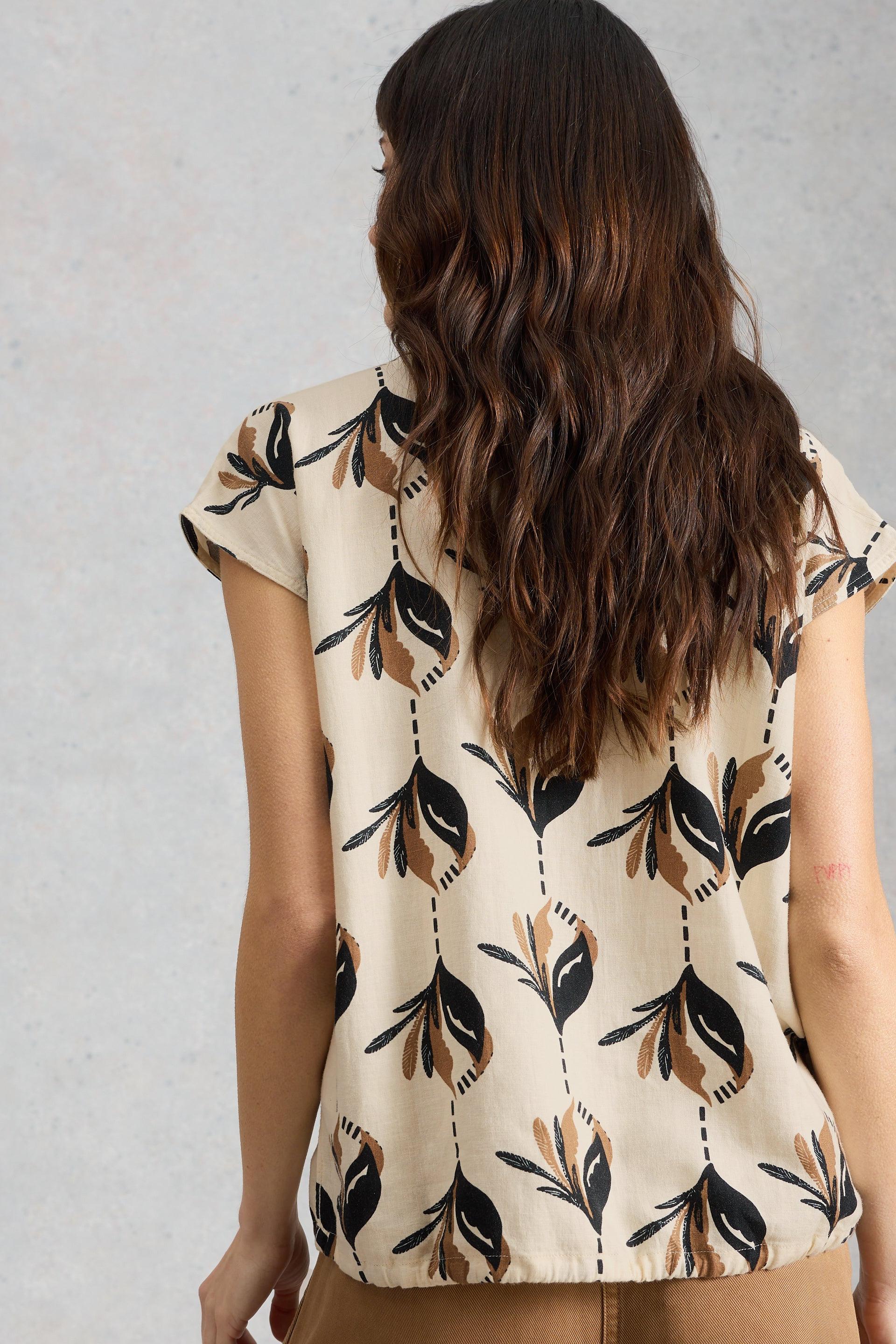 Woman wearing a sleeveless White Stuff top with leaf pattern on a plain background
