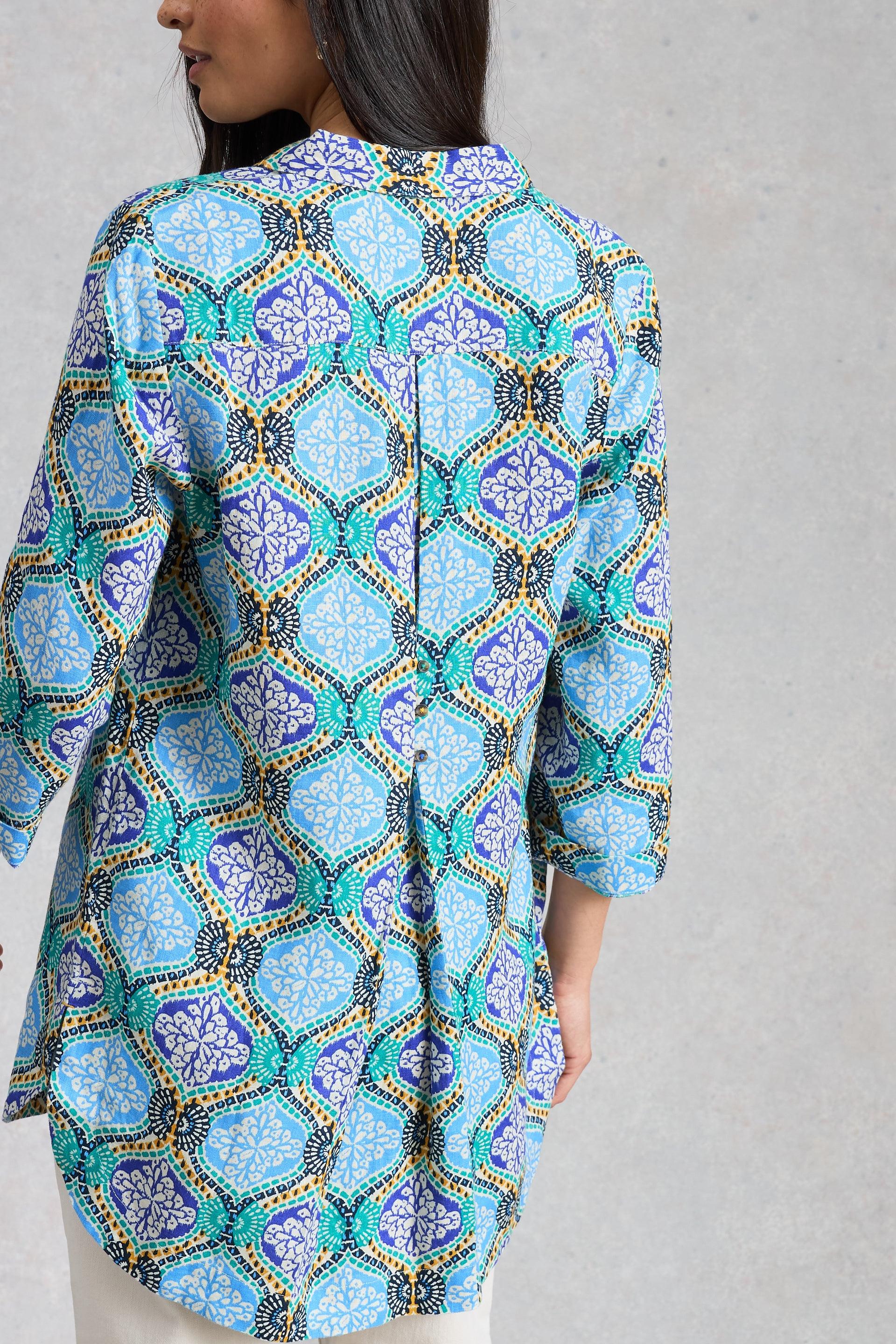 Woman wearing a patterned blue linen tunic with pleats against a gray background