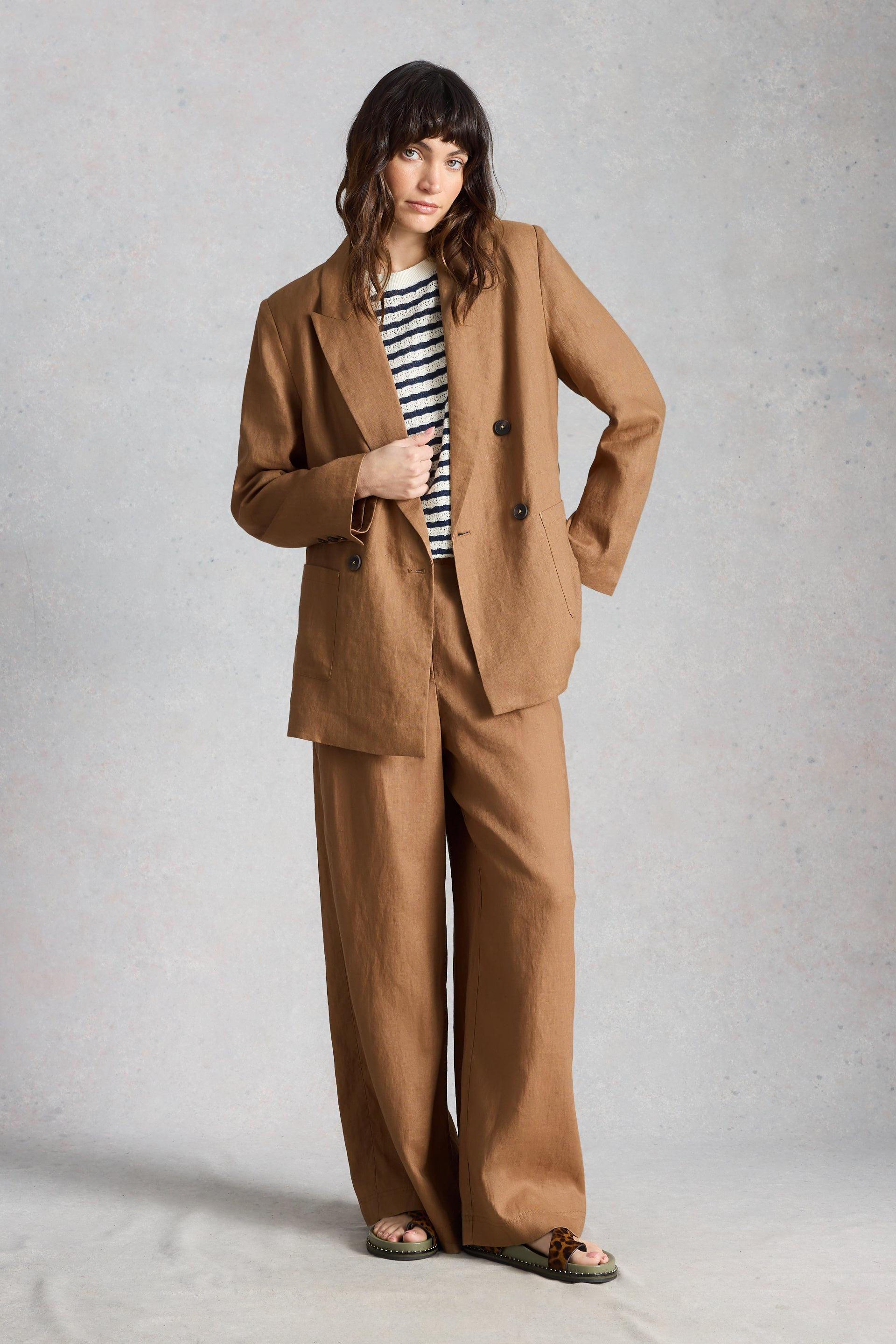 Woman wearing a brown linen suit with a striped shirt on a plain background