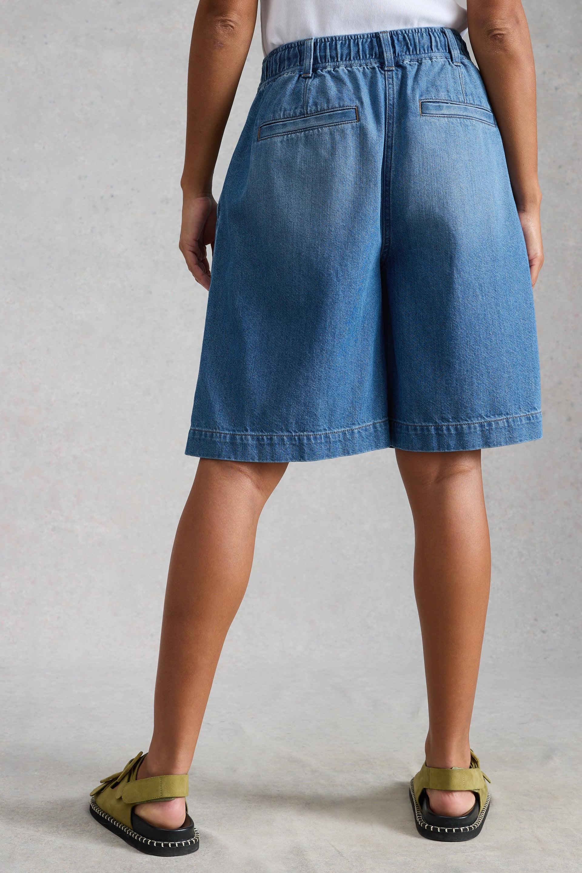Person wearing blue denim shorts on a neutral background