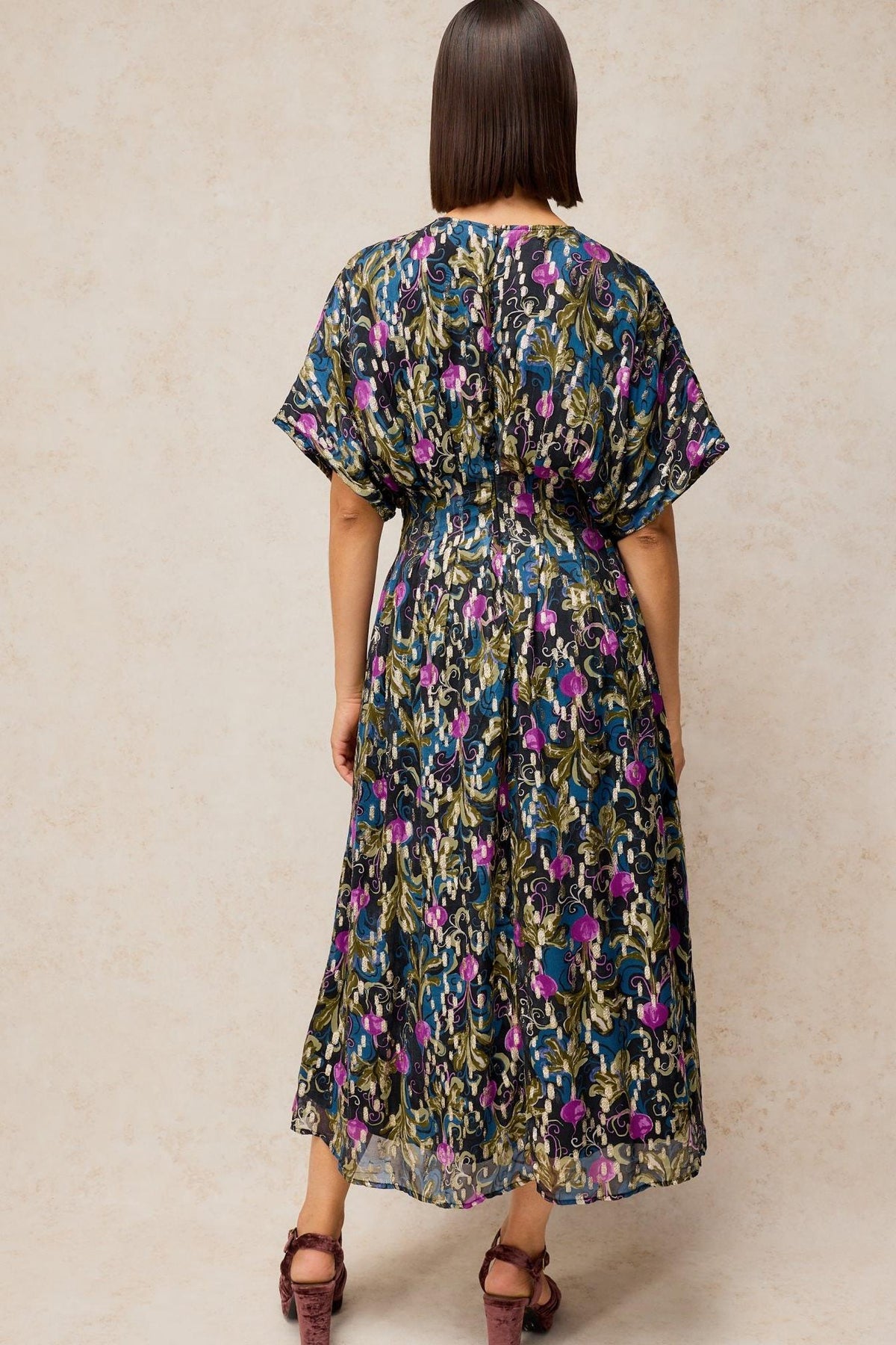 Rear view of a woman wearing a long, patterned viscose White Stuff occasion dress with short sleeves.