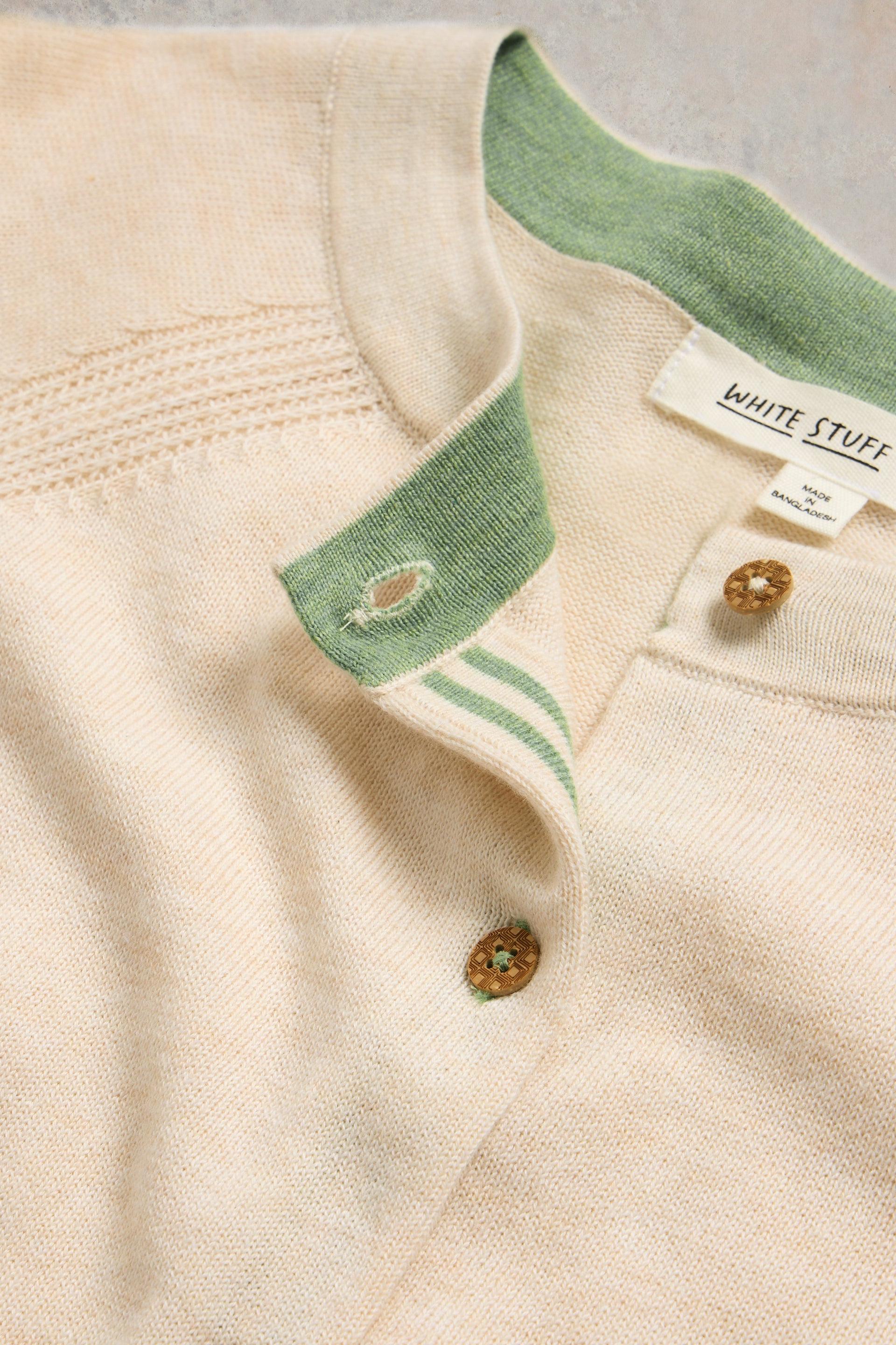 Close-up of a beige cardigan with green collar and buttons, featuring 'White Stuff' branding.