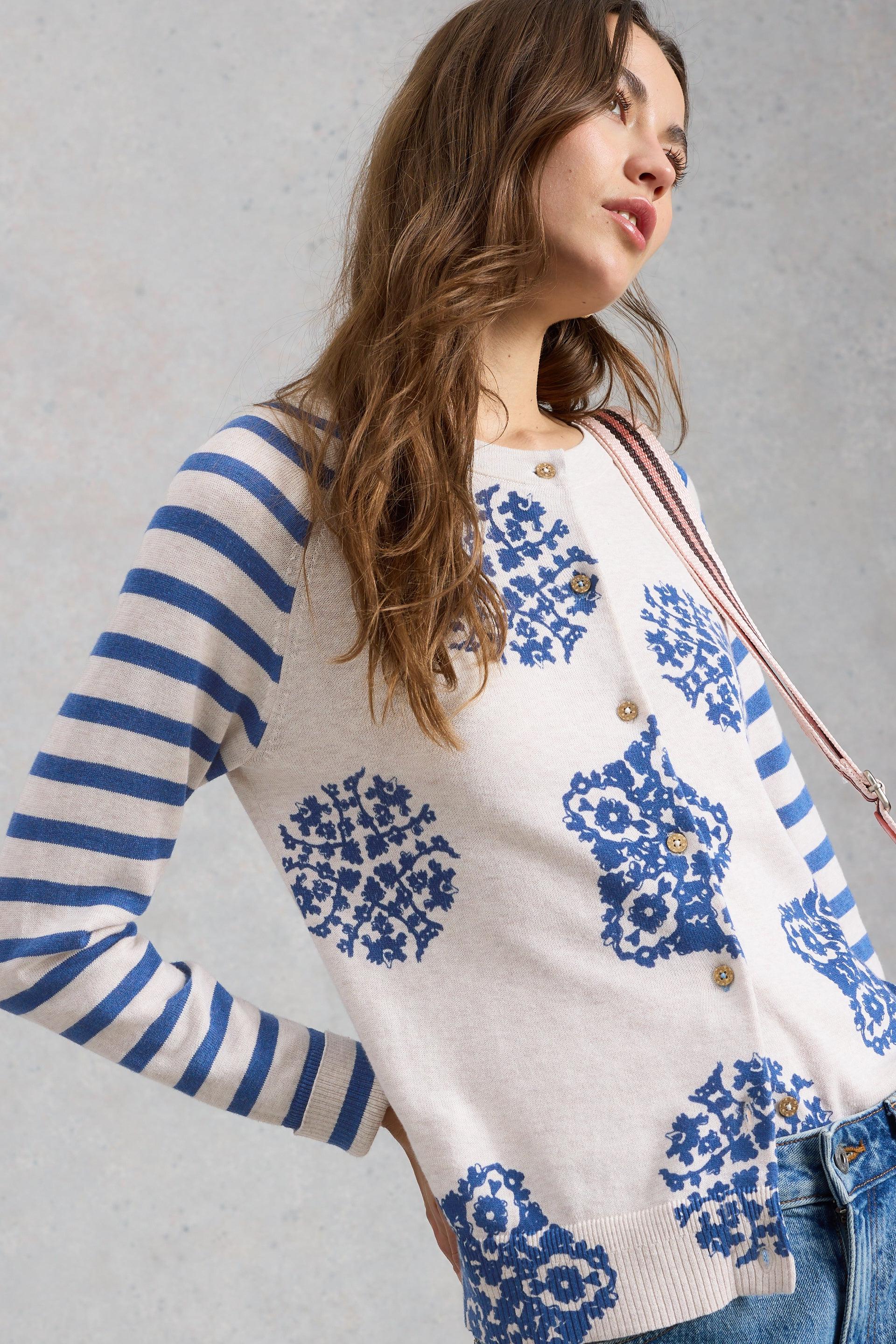 Woman wearing a white organic cotton cardigan with blue floral patterns and striped sleeves against a gray background