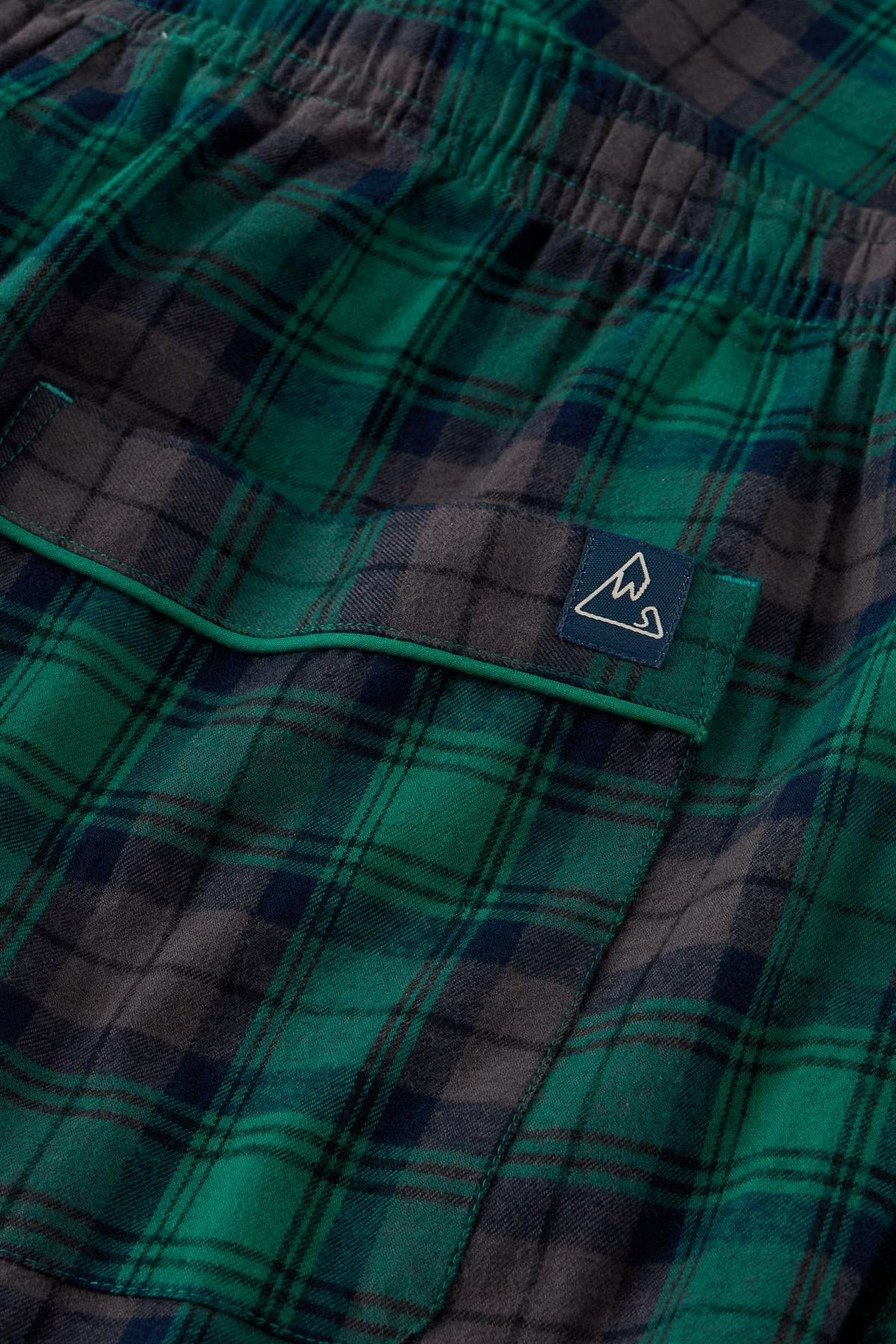 Close up of White Stuff men's green plaid cotton pyjama trousers with an elastic waistband and branded tab.
