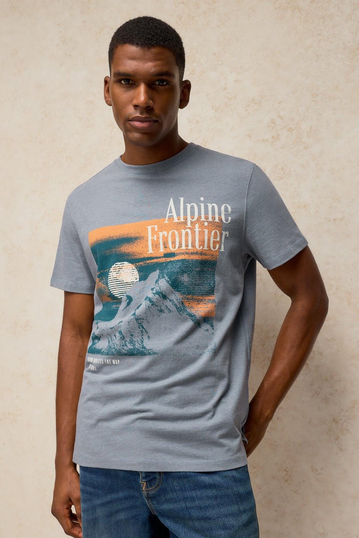 A man wearing a grey organic cotton t-shirt with an Alpine Frontier graphic print.