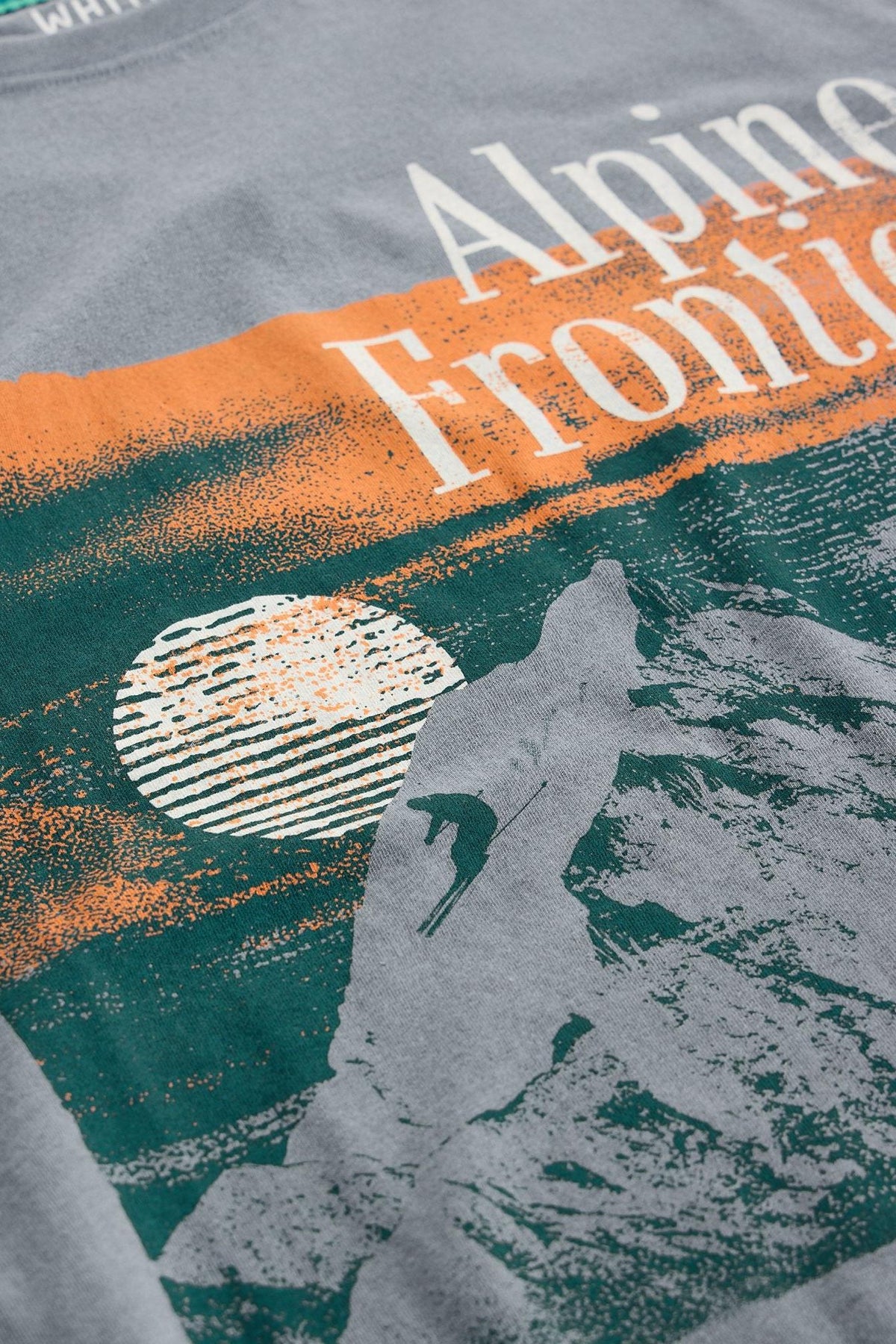 Close up of a White Stuff grey men's t-shirt featuring a screen-printed Alpine Frontier graphic with a skier.