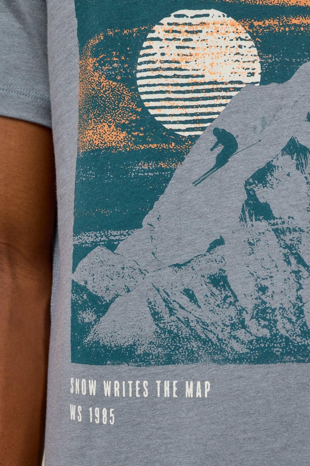 Close-up of a White Stuff grey organic cotton men's t-shirt featuring a graphic print of a skier on a mountain.