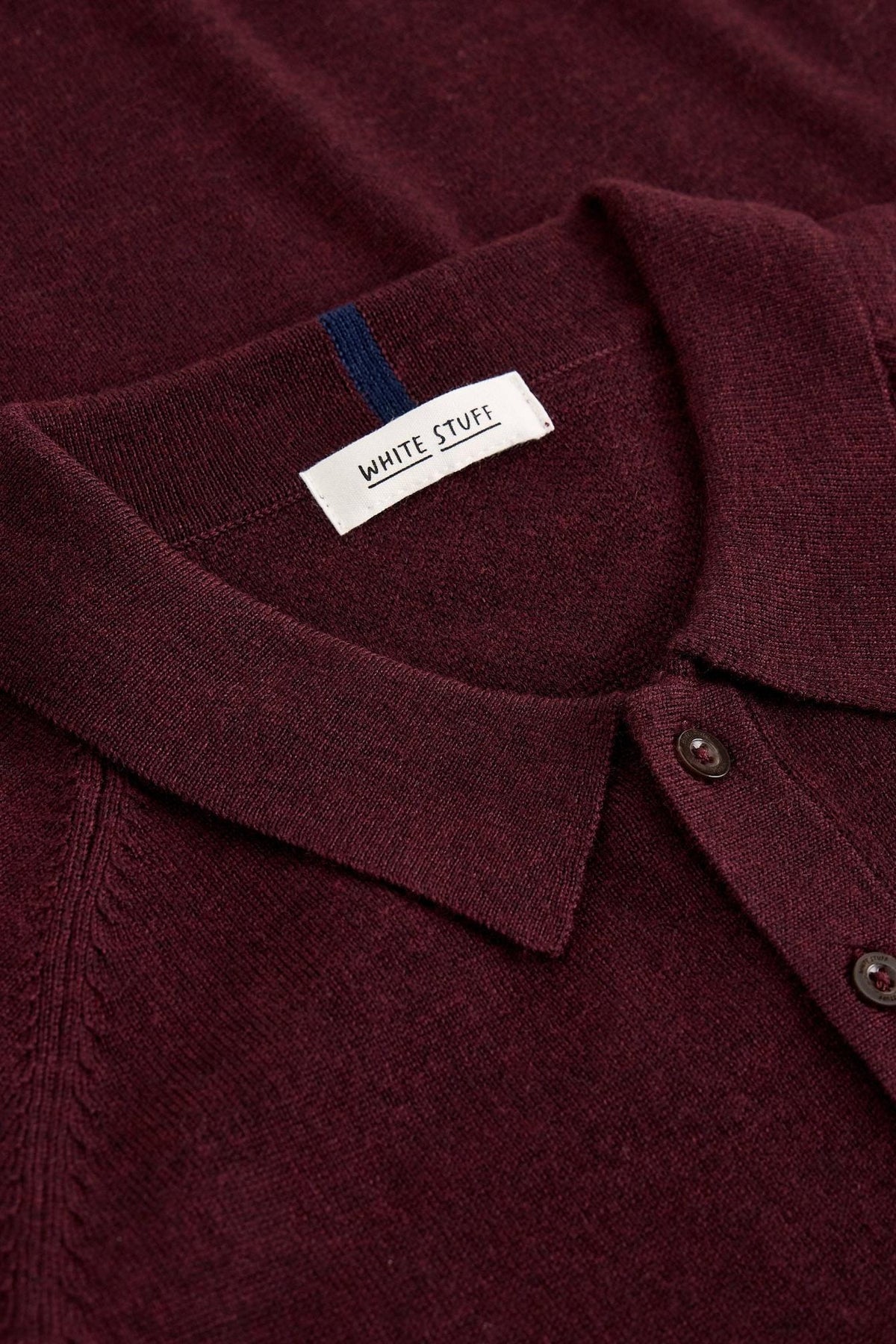 Close-up of a plum coloured White Stuff men's merino wool polo shirt showing the collar and brand label.