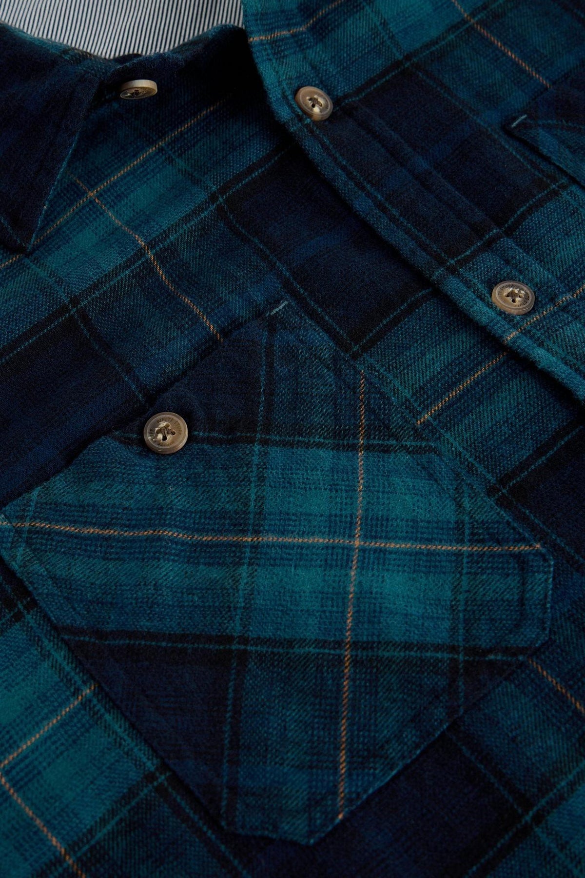 Close up of a White Stuff men's teal and blue plaid organic cotton long sleeve shirt with button details.