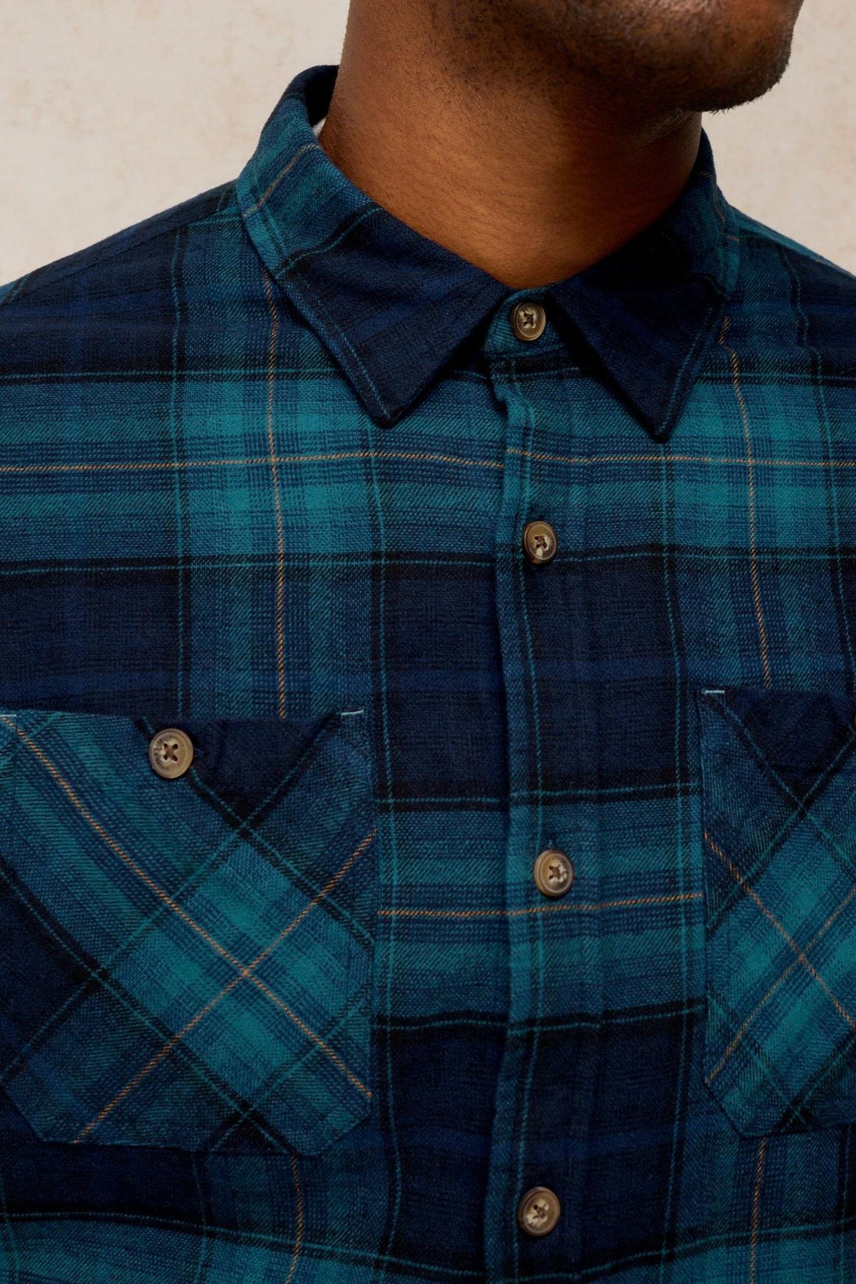 Close-up of a man wearing a teal and blue plaid long sleeve organic cotton shirt by White Stuff.