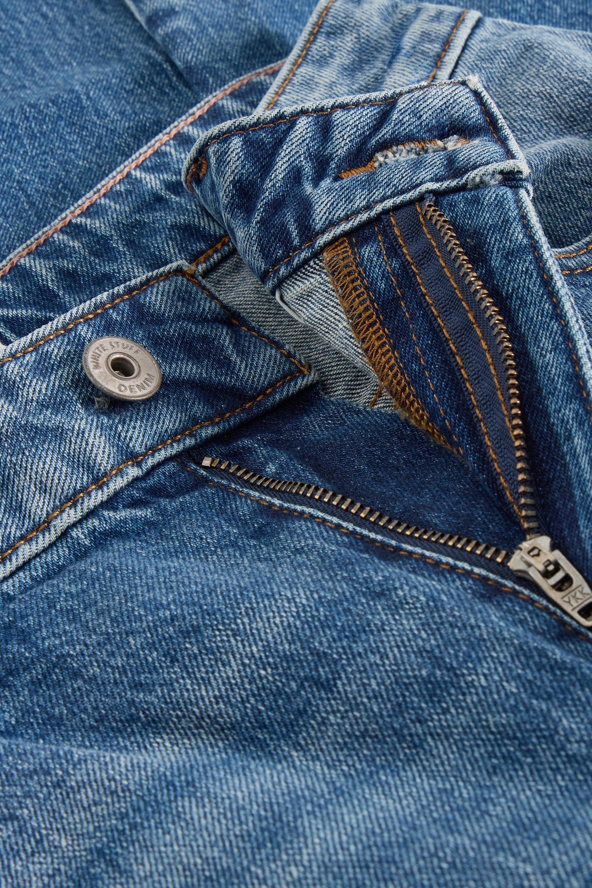 Close-up of a White Stuff mid denim jeans fly showing the silver metal button and YKK zipper detail.