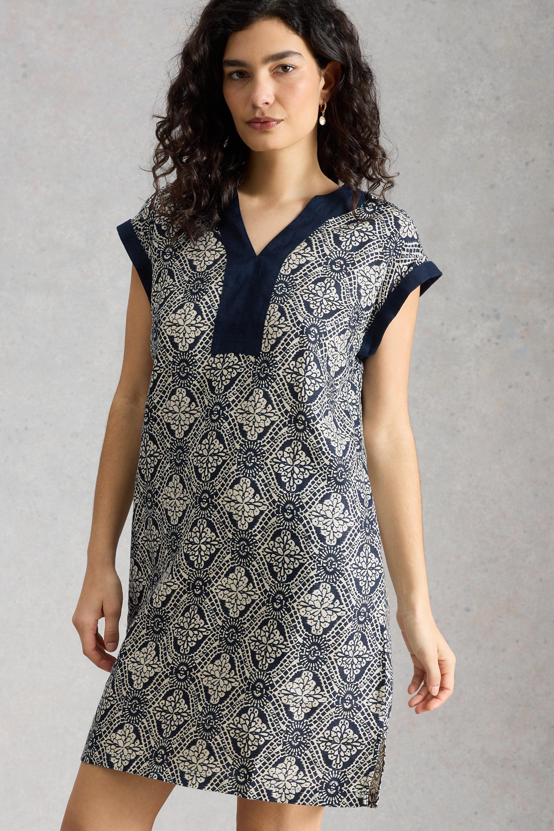 Woman wearing a patterned navy linen dress with a plain background
