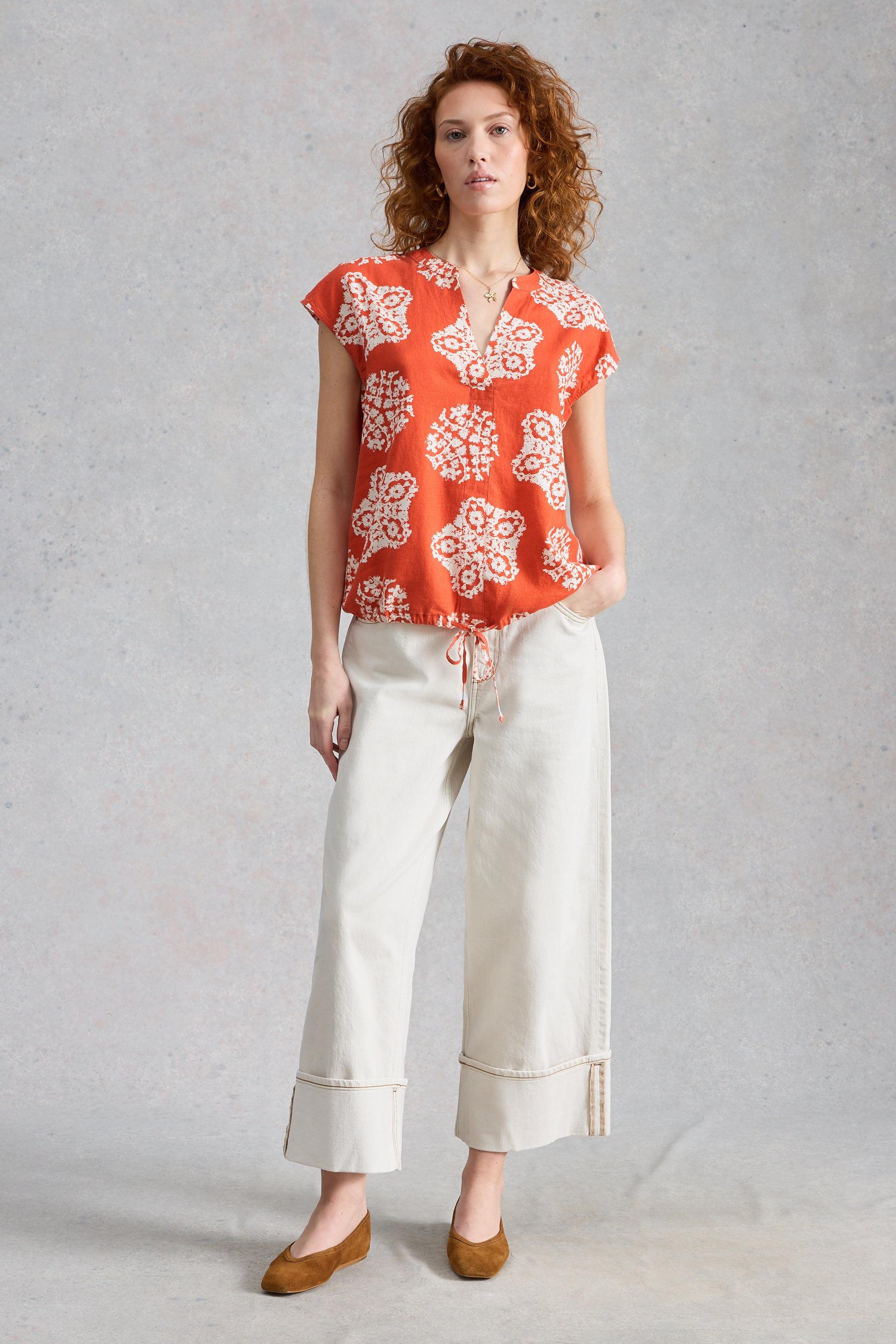 Woman wearing a red linen blouse and white pants on a gray background