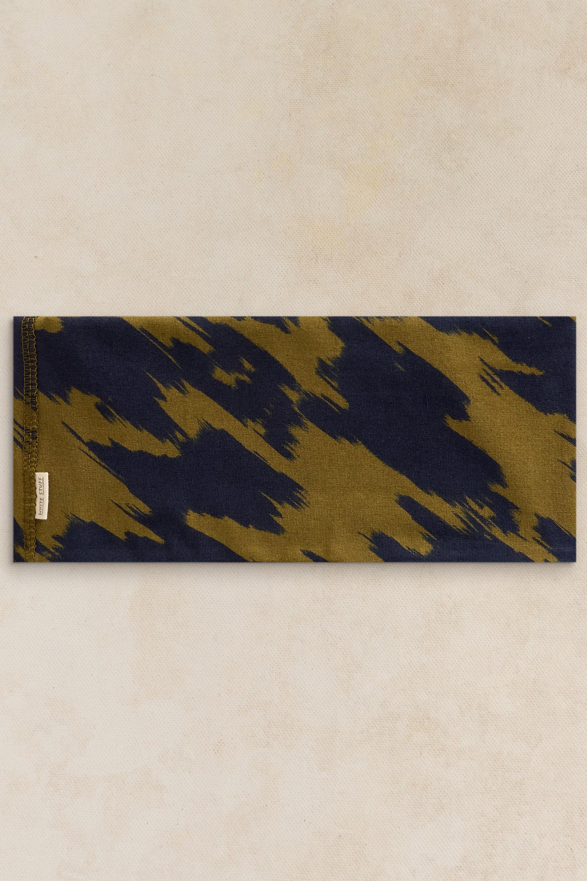 A rectangular fabric headband featuring a navy and olive green abstract brushstroke pattern with a White Stuff brand label