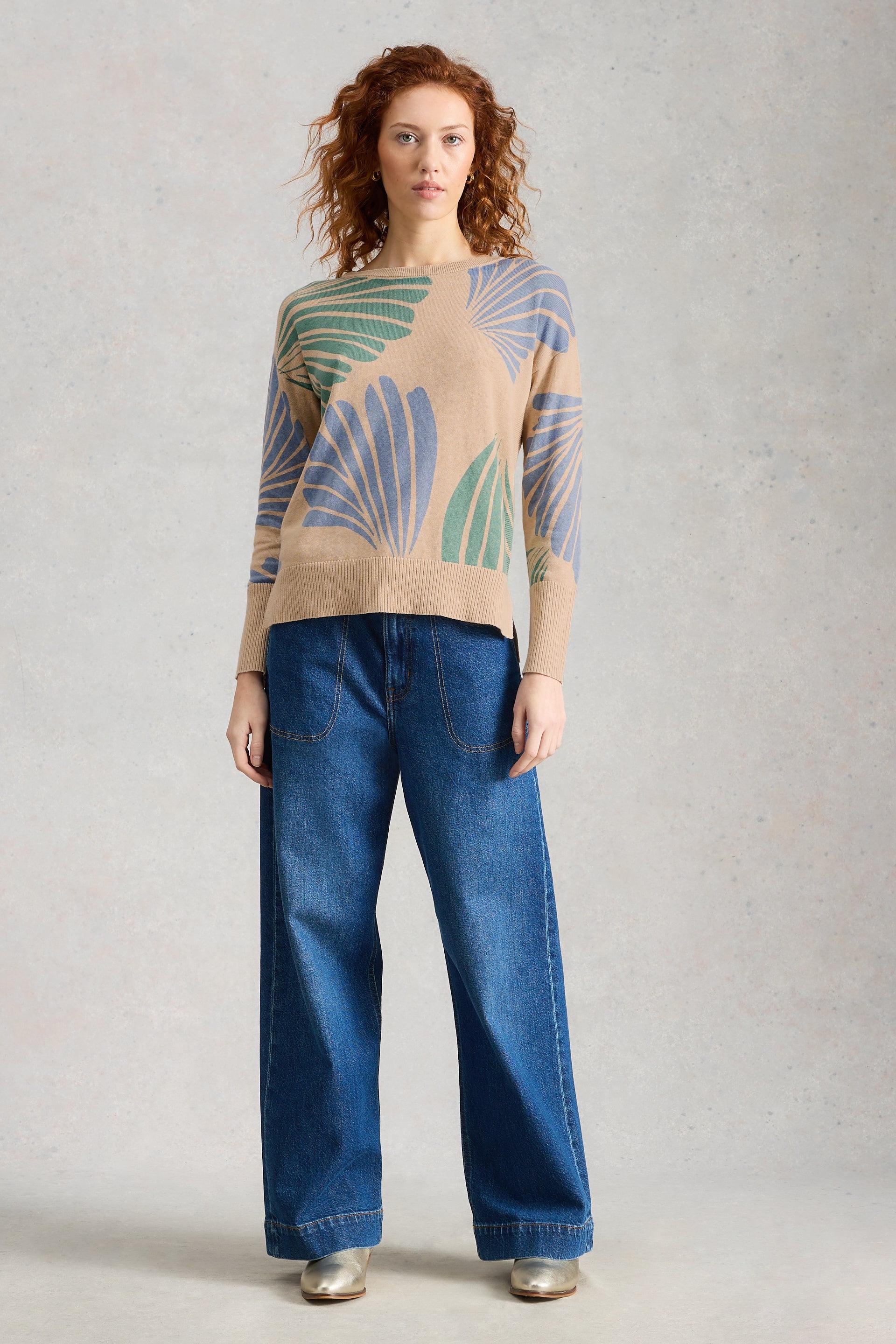 Woman wearing a patterned White Stuff sweater and blue jeans on a plain background