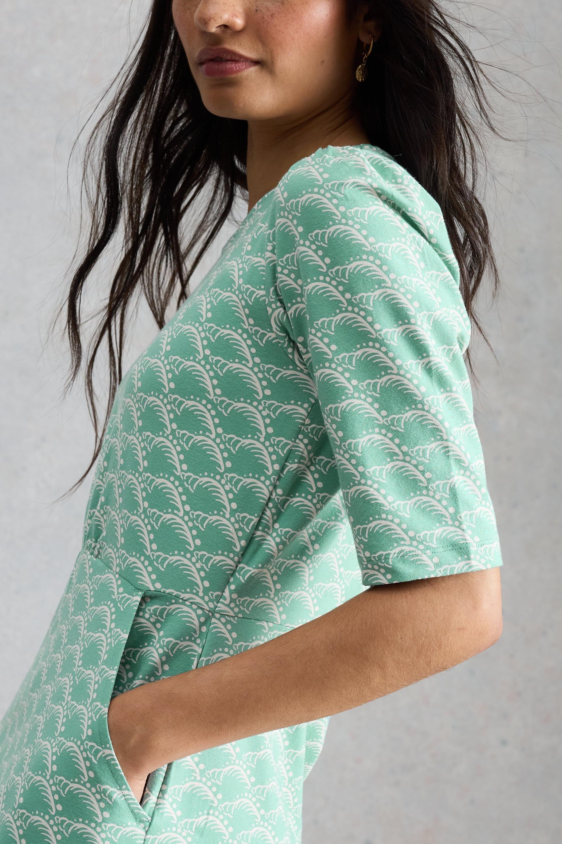 Woman wearing a green White Stuff dress against a gray background