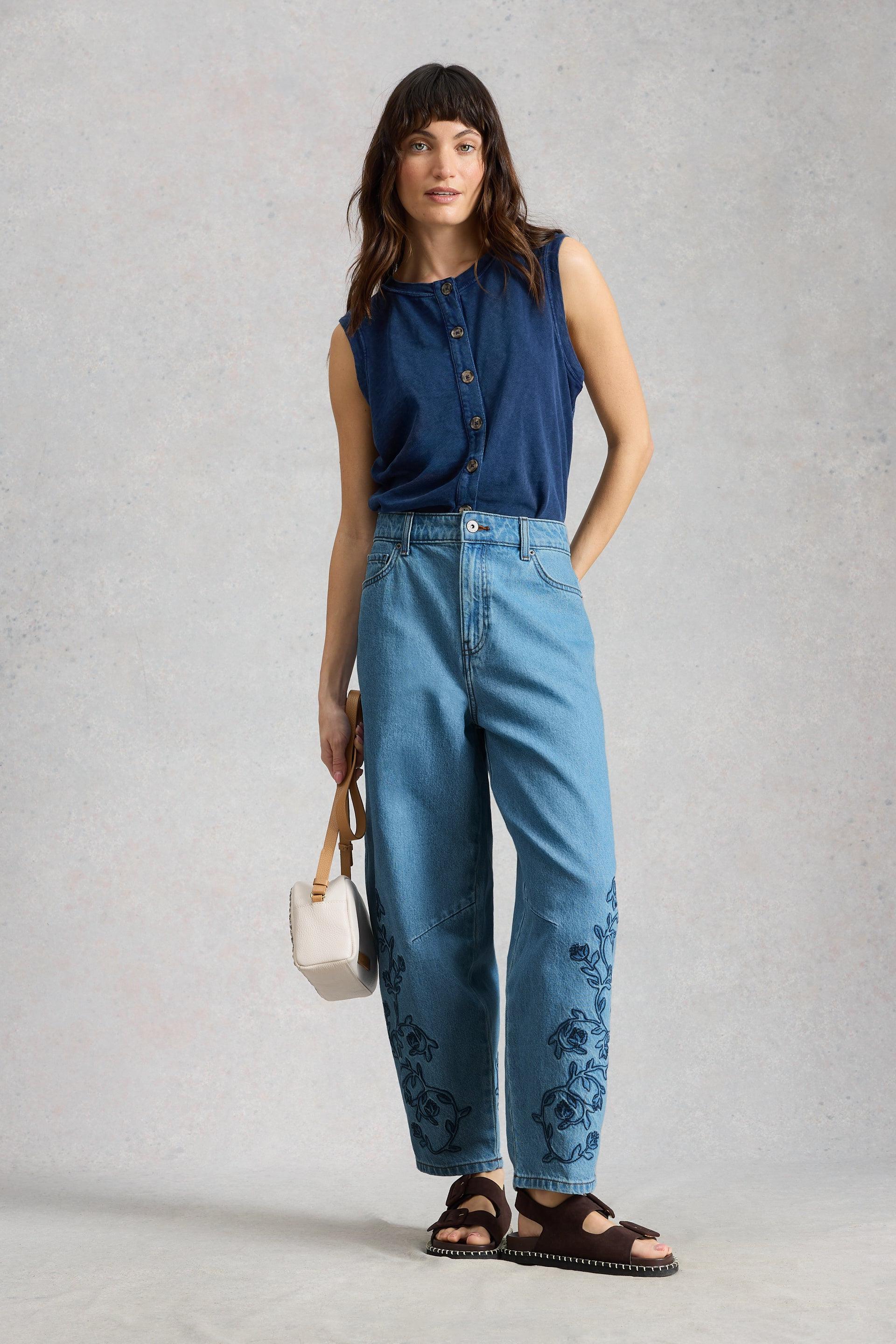 Woman wearing a navy sleeveless top and barrel leg jeans, standing against a plain background