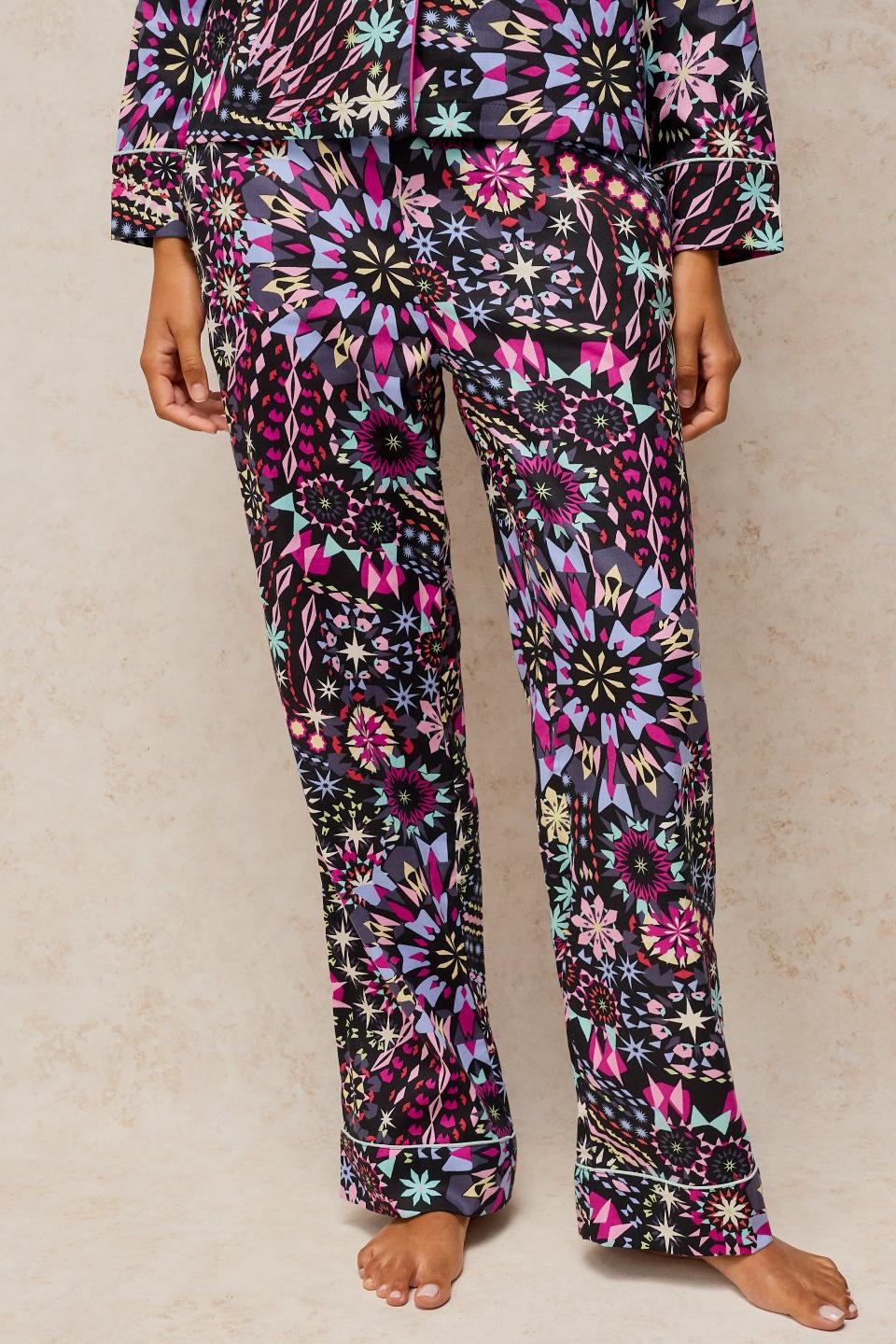Person wearing White Stuff black print organic cotton pyjama bottoms with a vibrant geometric floral pattern.