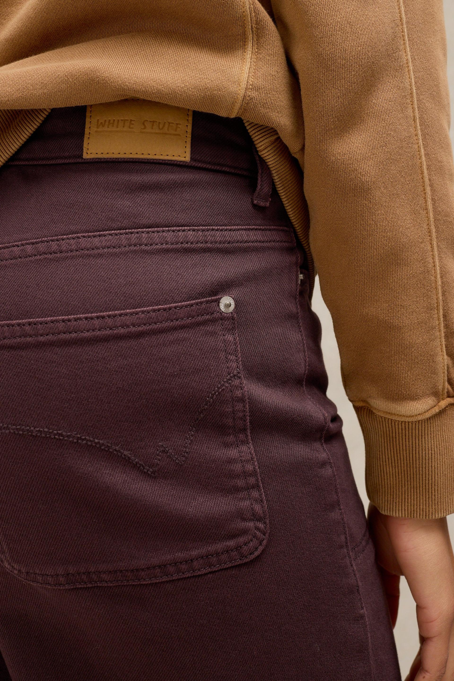 Close-up of burgundy organic cotton jeans with a White Stuff label and tan sweatshirt