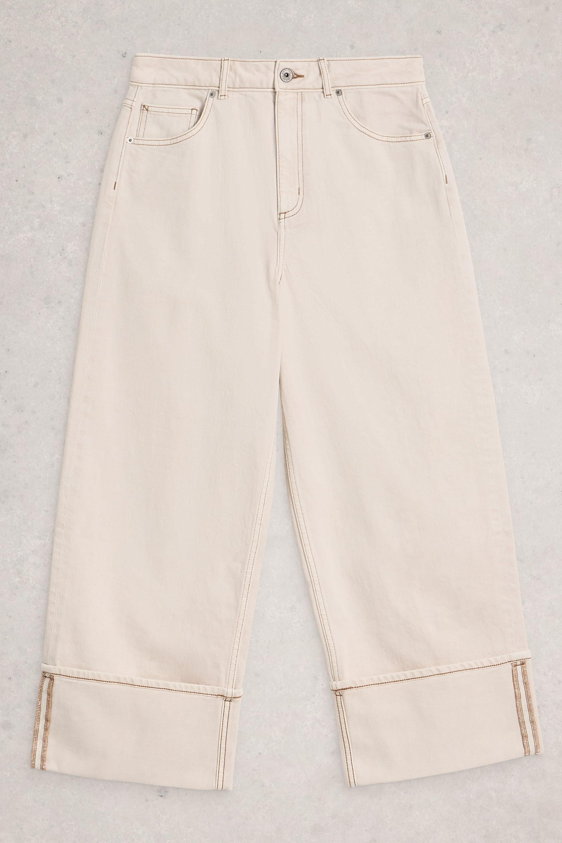 Cream-colored wide-leg White Stuff trousers made from organic cotton, flat-laid on a grey textured background.