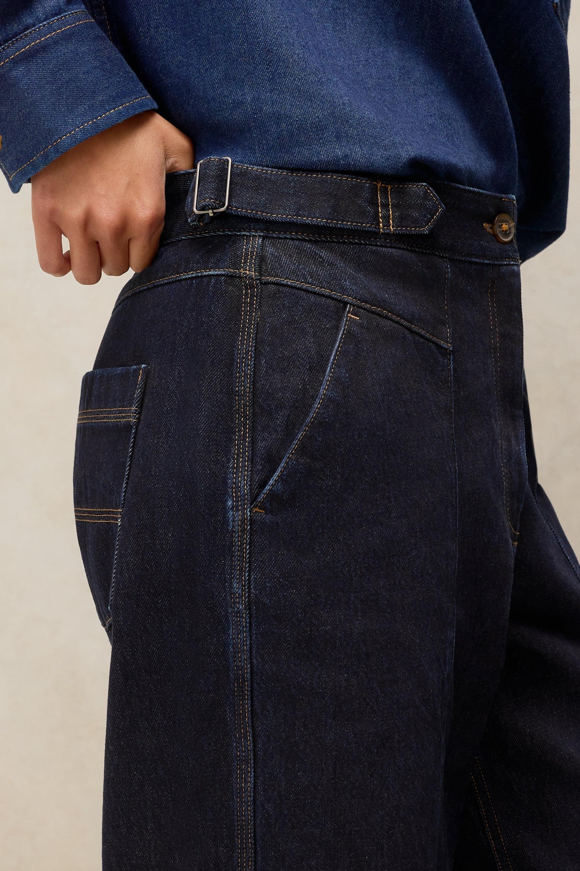 Close-up of a person wearing White Stuff organic cotton dark denim trousers with a side buckle detail.