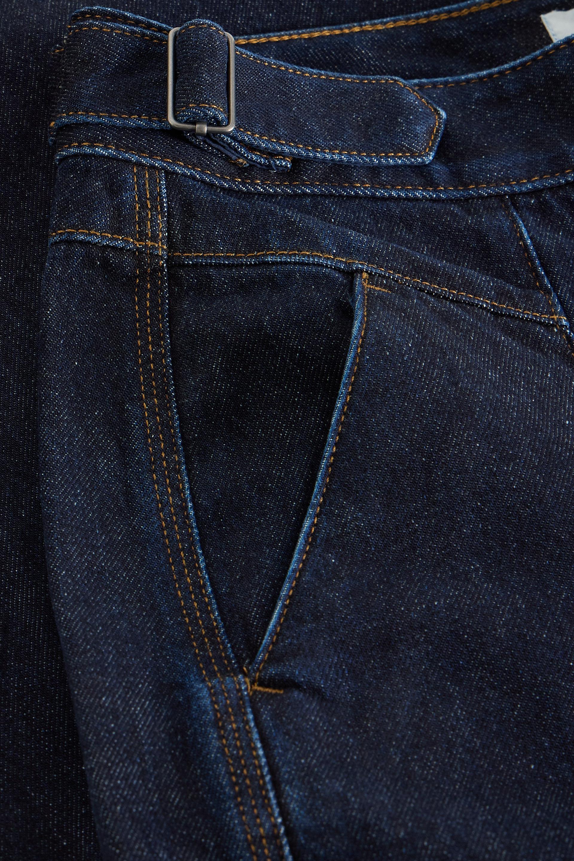 Close up of a White Stuff organic cotton dark denim waistband with a side buckle adjuster
