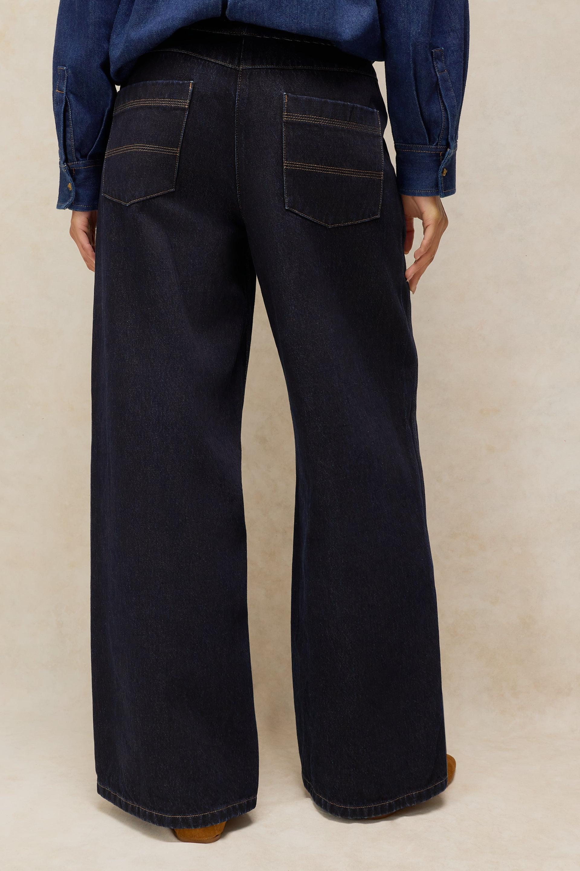 Back view of a person wearing dark wash organic cotton wide-leg jeans from White Stuff with a denim shirt.