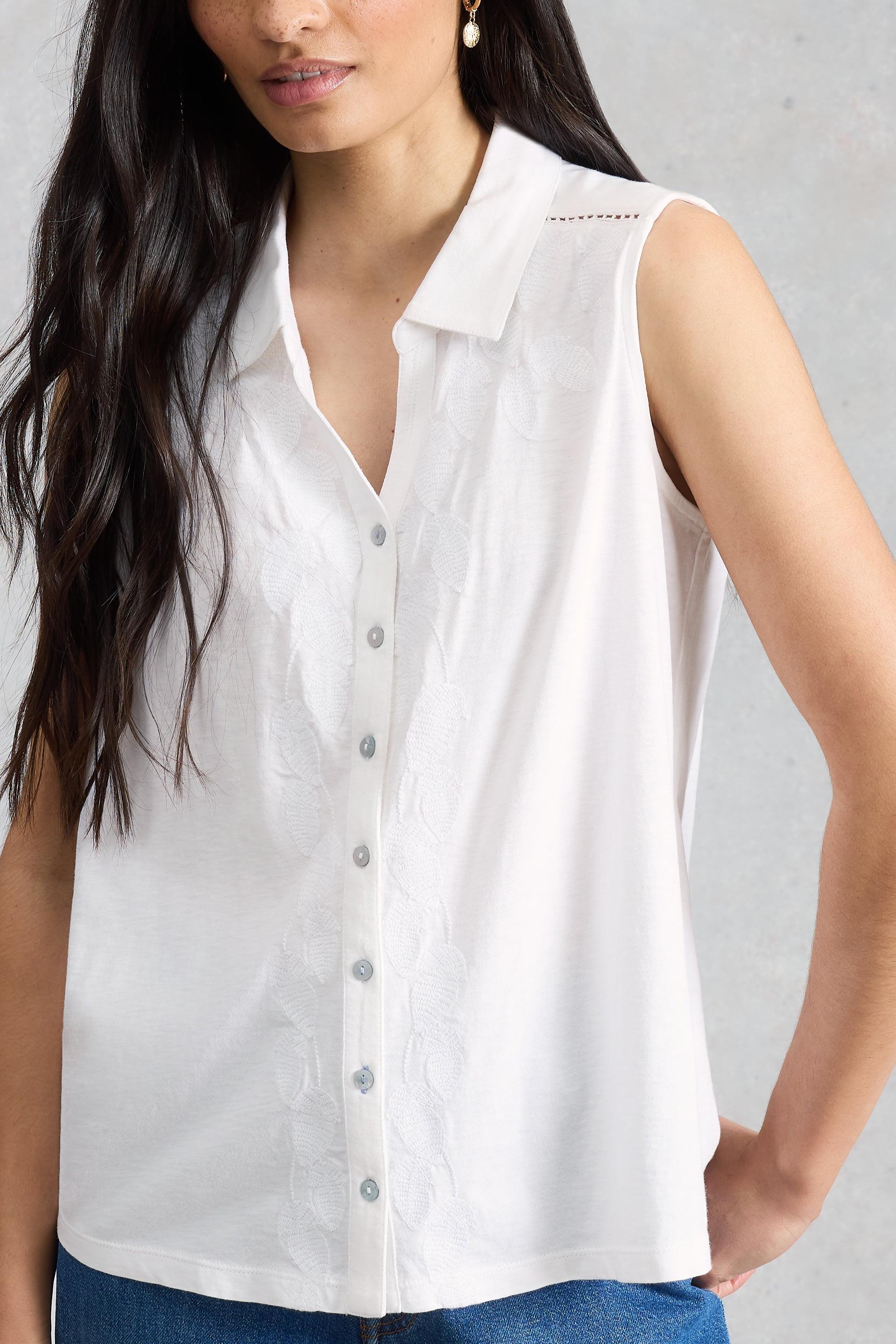 Woman wearing a white sleeveless button-up shirt against a gray background