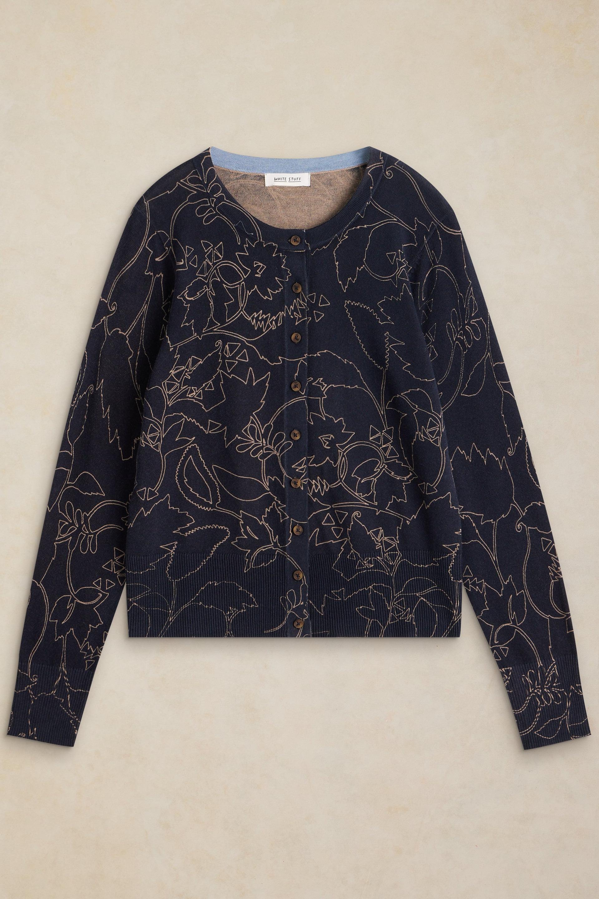 A navy blue cropped cardigan sweater with a beige floral line pattern, laid flat against a textured beige background.