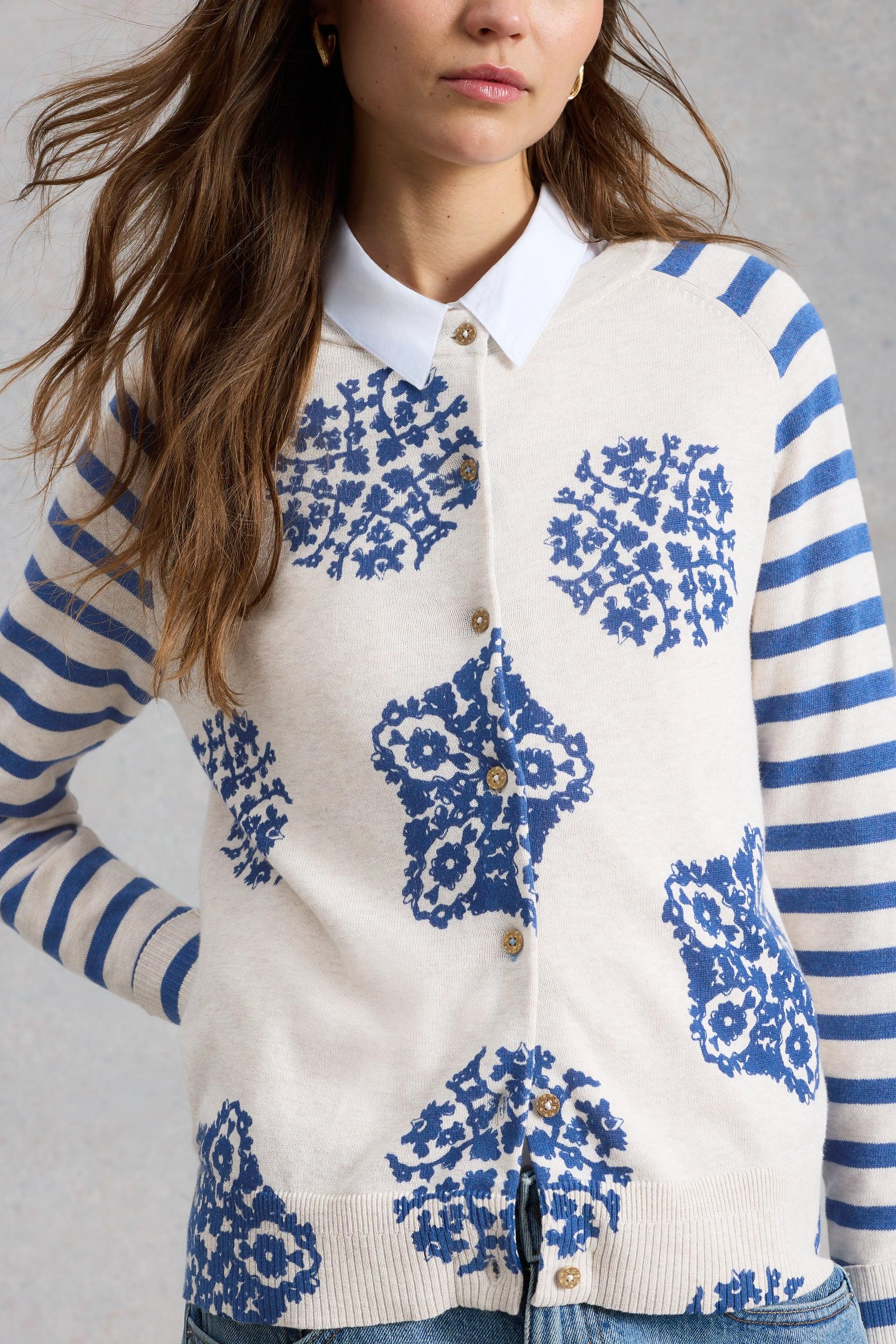 Person wearing a white cardigan with blue floral patterns and striped sleeves on a gray background