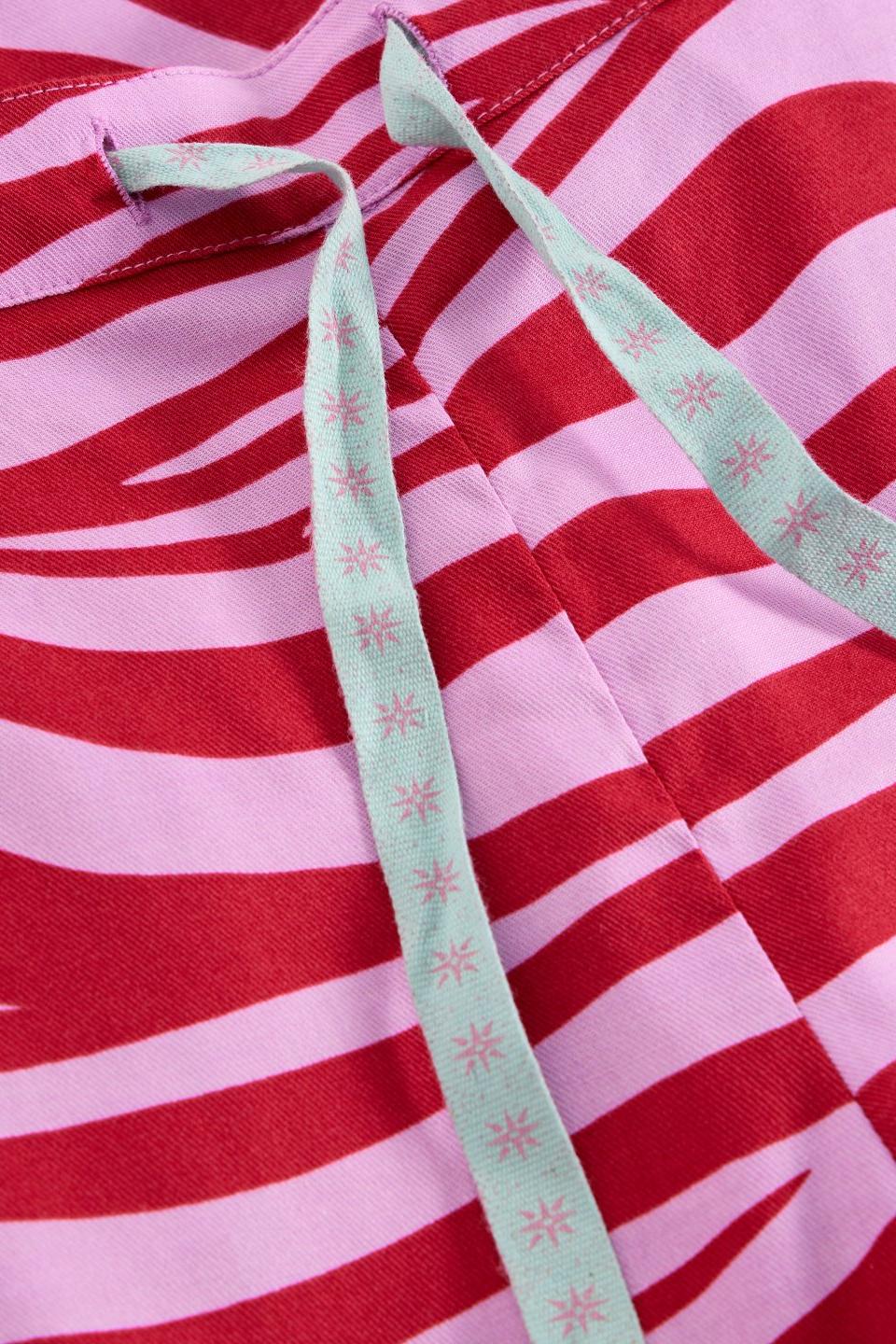 Close up of White Stuff organic cotton pyjama bottoms featuring a pink and red abstract zebra-style print and drawstring.
