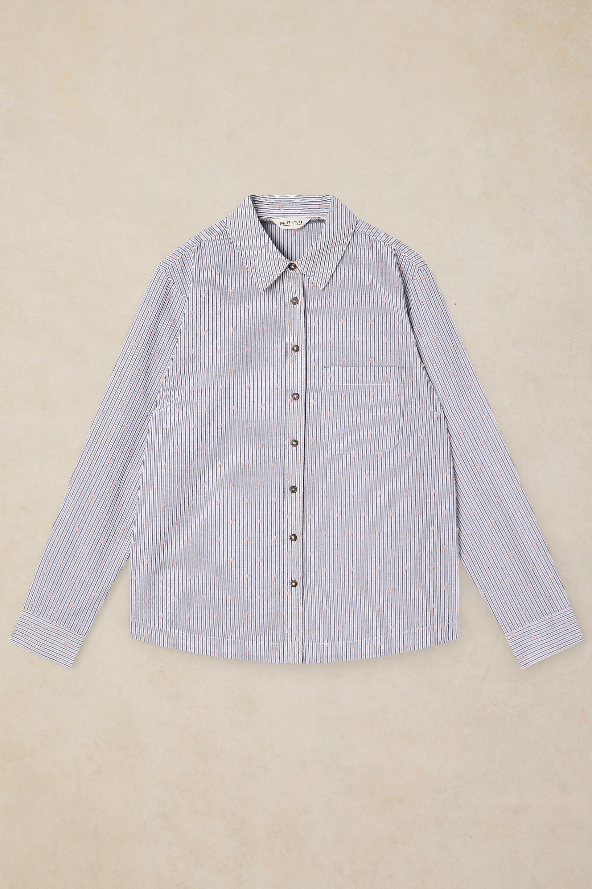 A long-sleeve button-up shirt with a fine vertical stripe pattern in light blue and white, laid flat against a textured beige background.