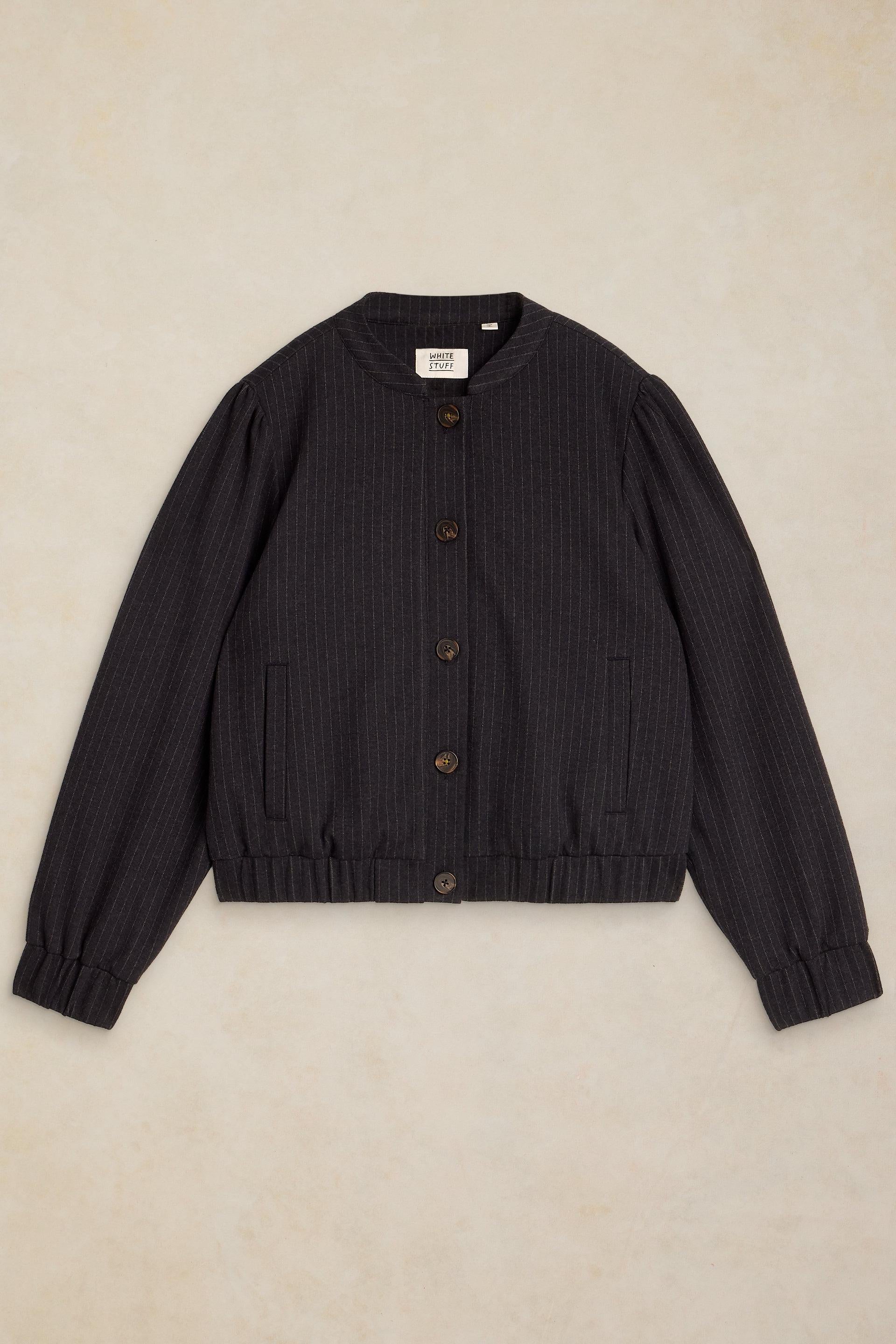 A navy pinstripe bomber jacket with brown buttons, laid flat on a textured beige background.